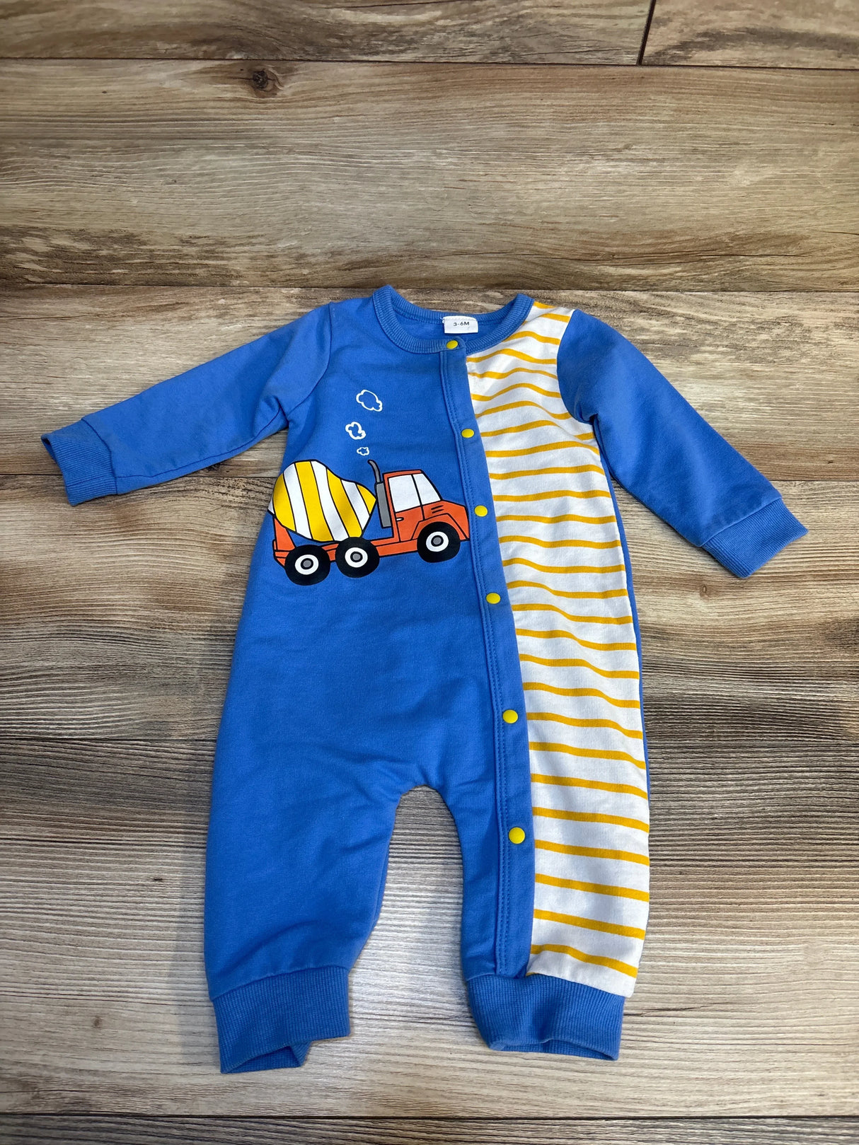 Blue baby romper with yellow striped panel and cement truck graphic on wooden floor