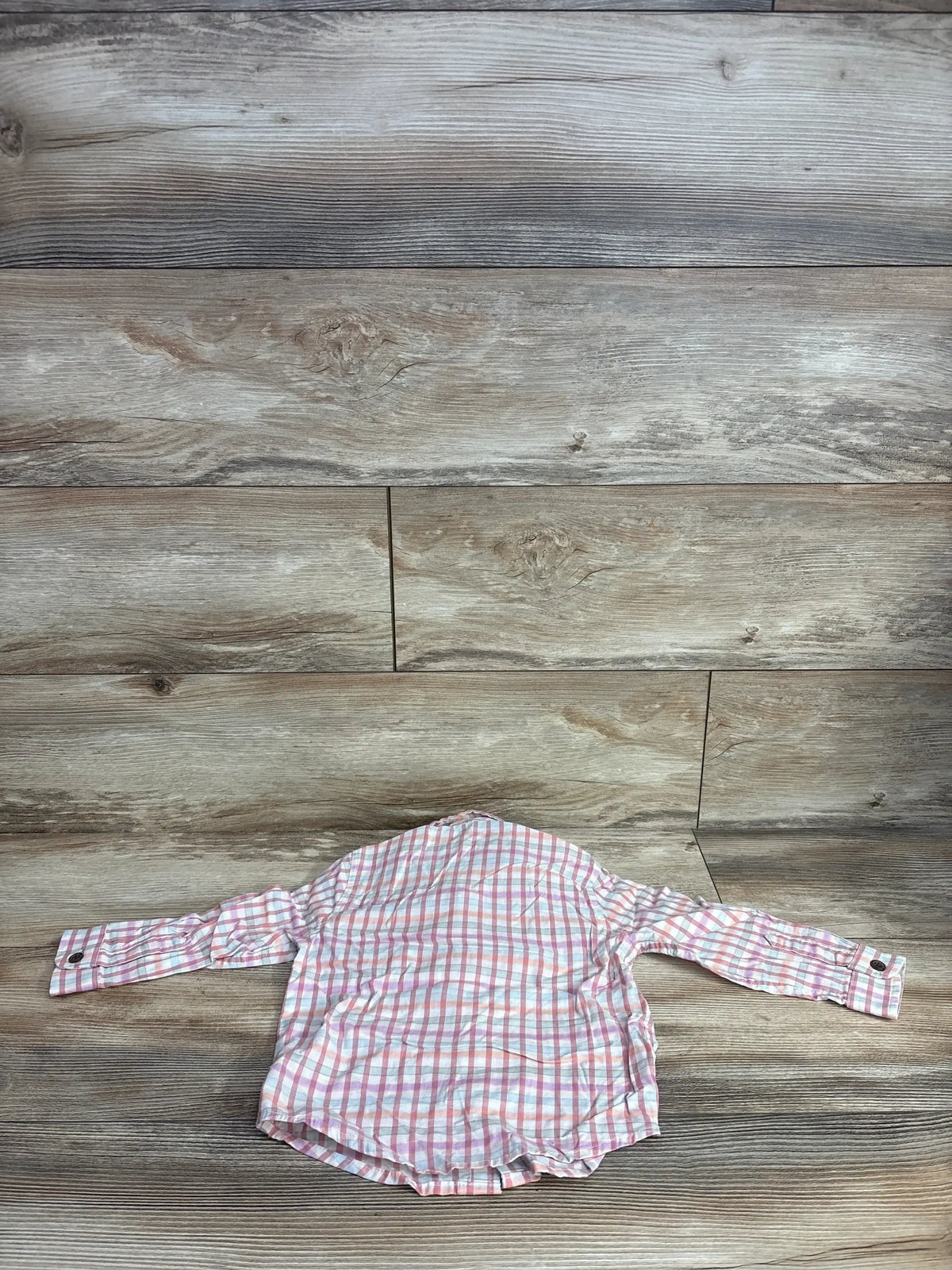 Pink and white plaid long sleeve button-up shirt for kids on wood background