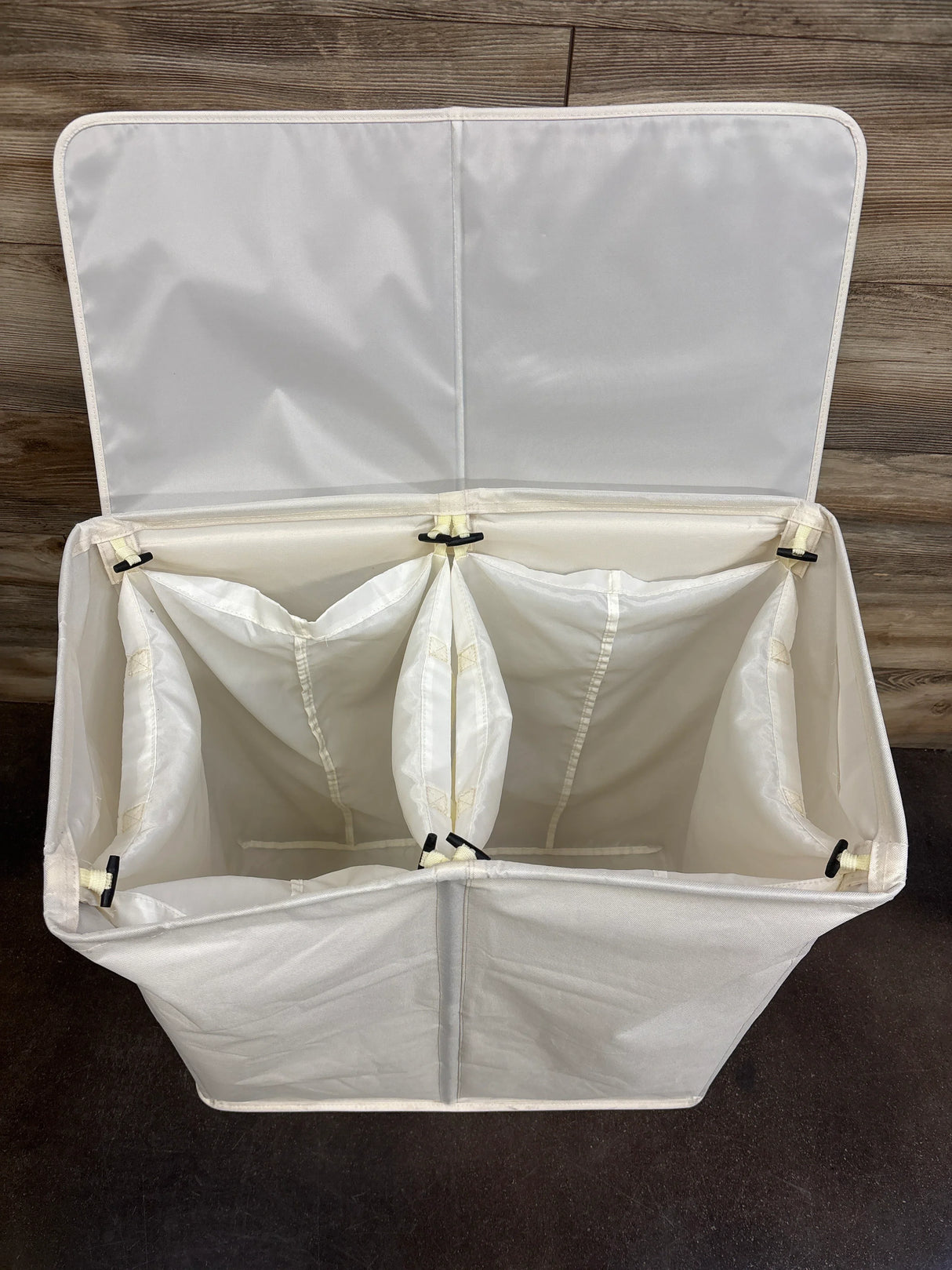 Top view of double laundry hamper with lid open showing two fabric compartments and dividers on wood background