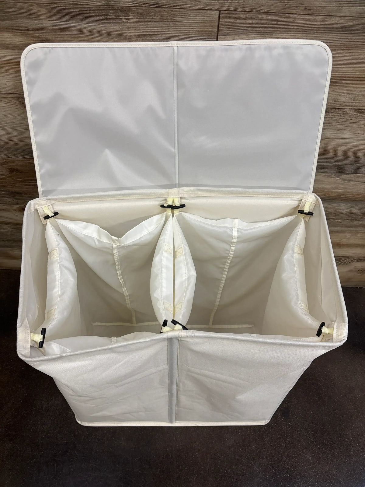 Top view of double laundry hamper with lid open showing two fabric compartments and dividers on wood background