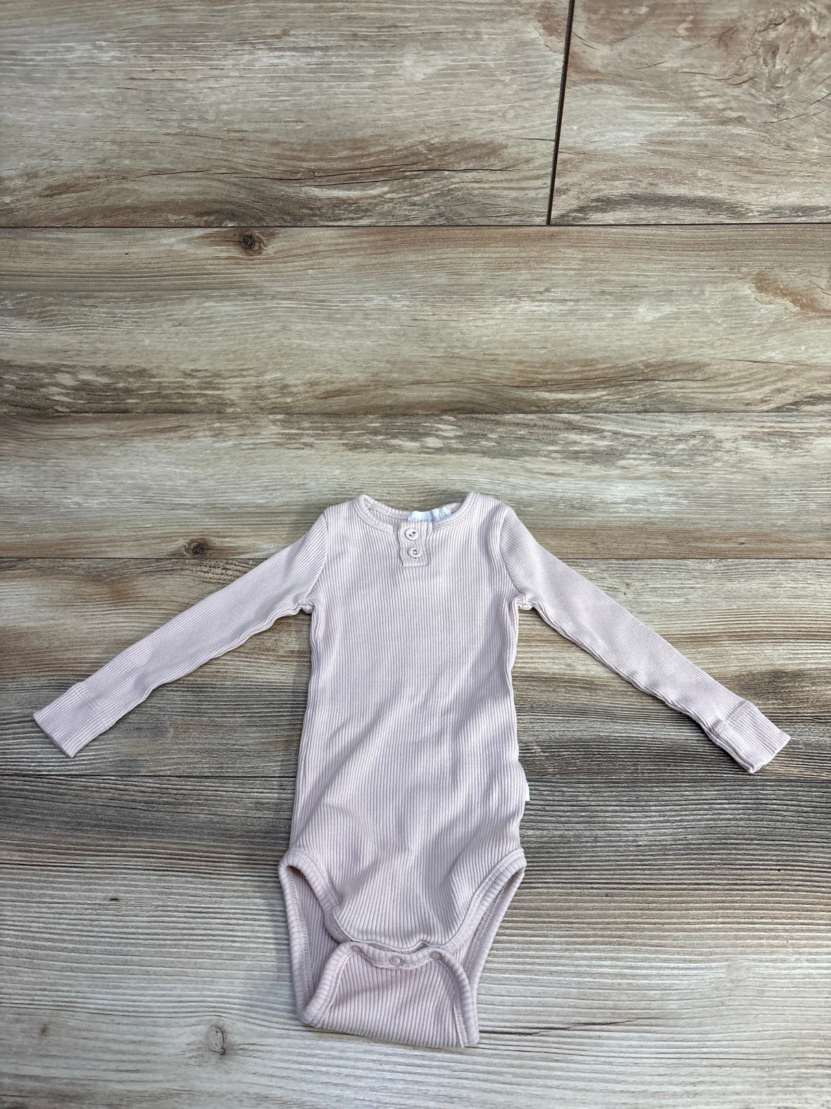 Light pink long-sleeve ribbed baby onesie with button detail on wooden floor