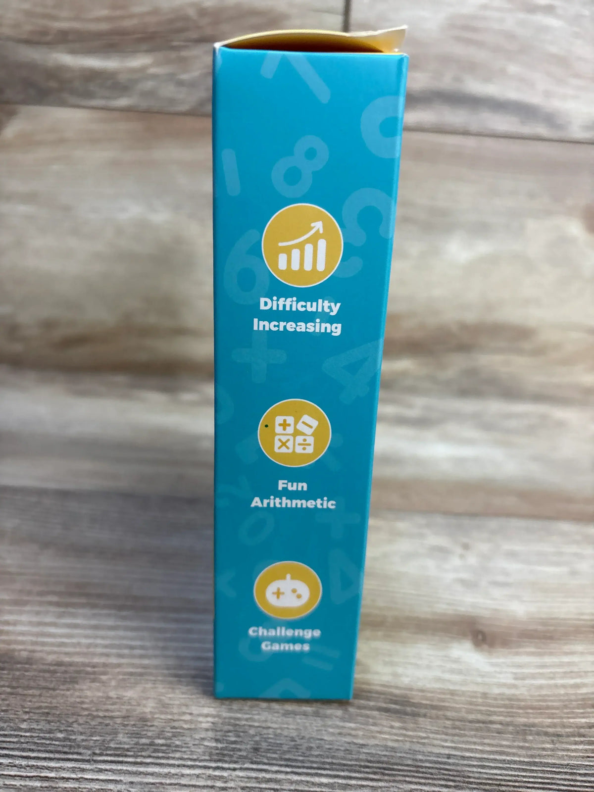 Side view of Alilo Math Magic Portable Math Games 3 plus box showing printed text Difficulty Increasing, Fun Arithmetic, Challenge Games on wood surface