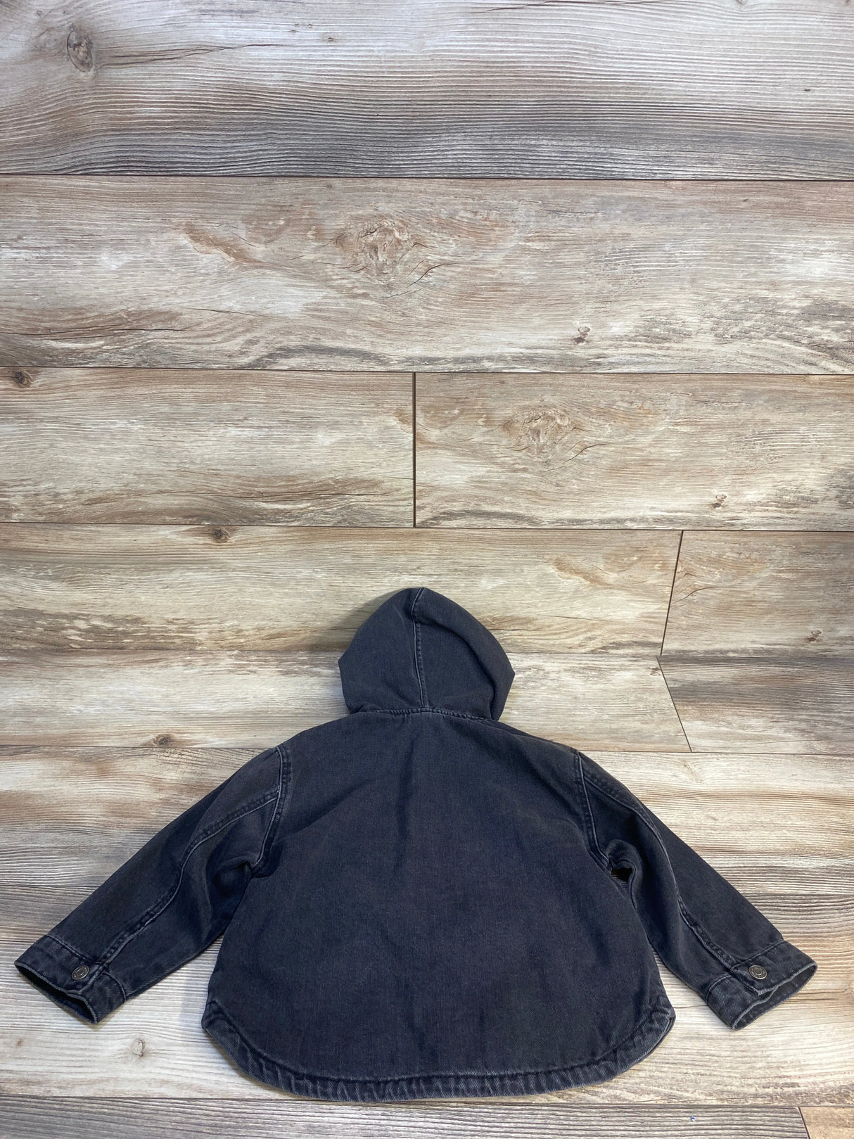 Black denim kids hooded jacket with long sleeves laid flat on wood background