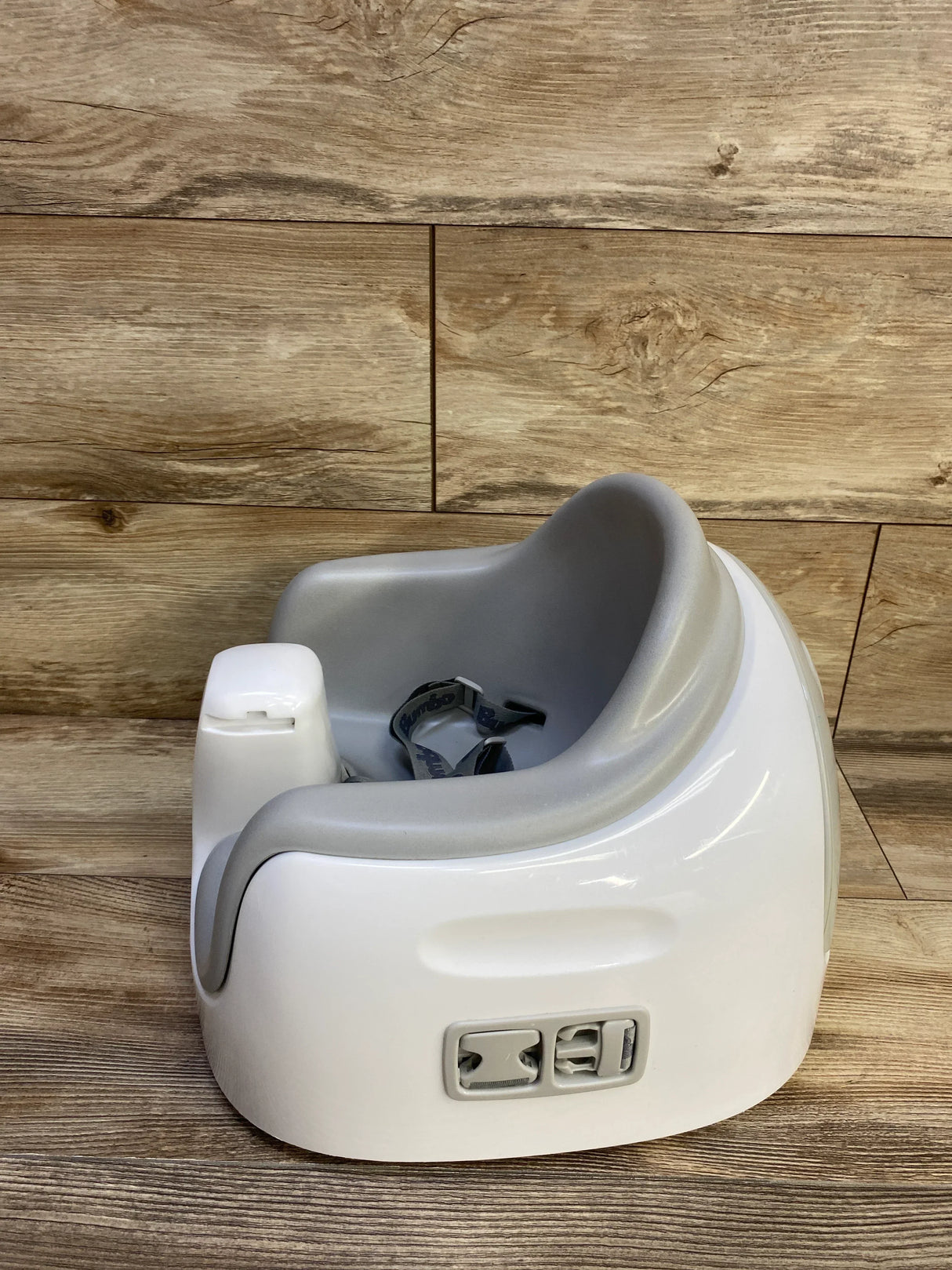 Three-quarter view of Bumbo Multi Seat showing grey padded insert, removable tray and straps on wood background