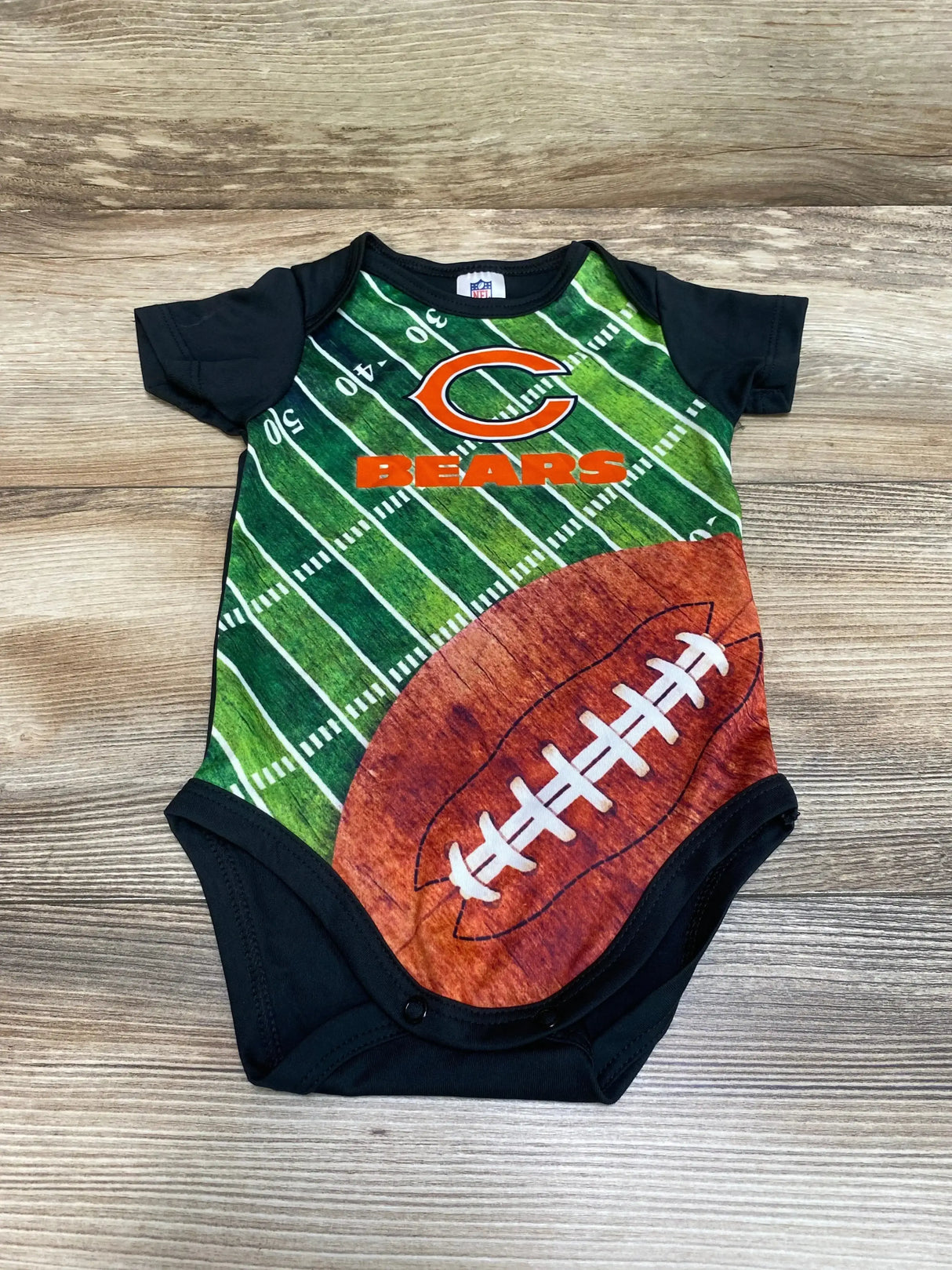Flat lay of black Chicago Bears baby bodysuit (3 to 6 months) showing printed football field, large football graphic and Bears logo on wood background