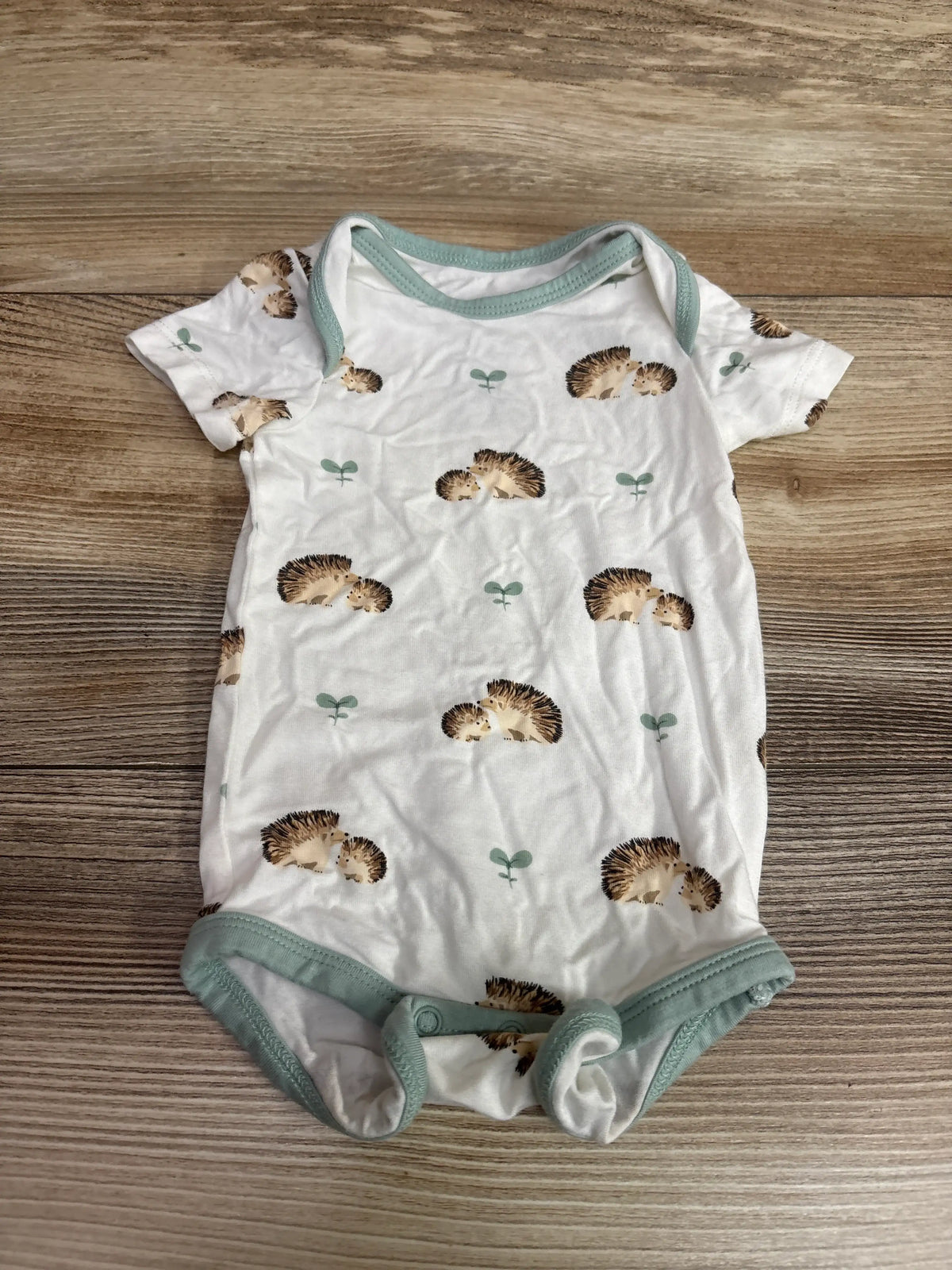 Front view of Kyte Baby bamboo hedgehog bodysuit in white with sage trim, hedgehog print, and snaps on wood