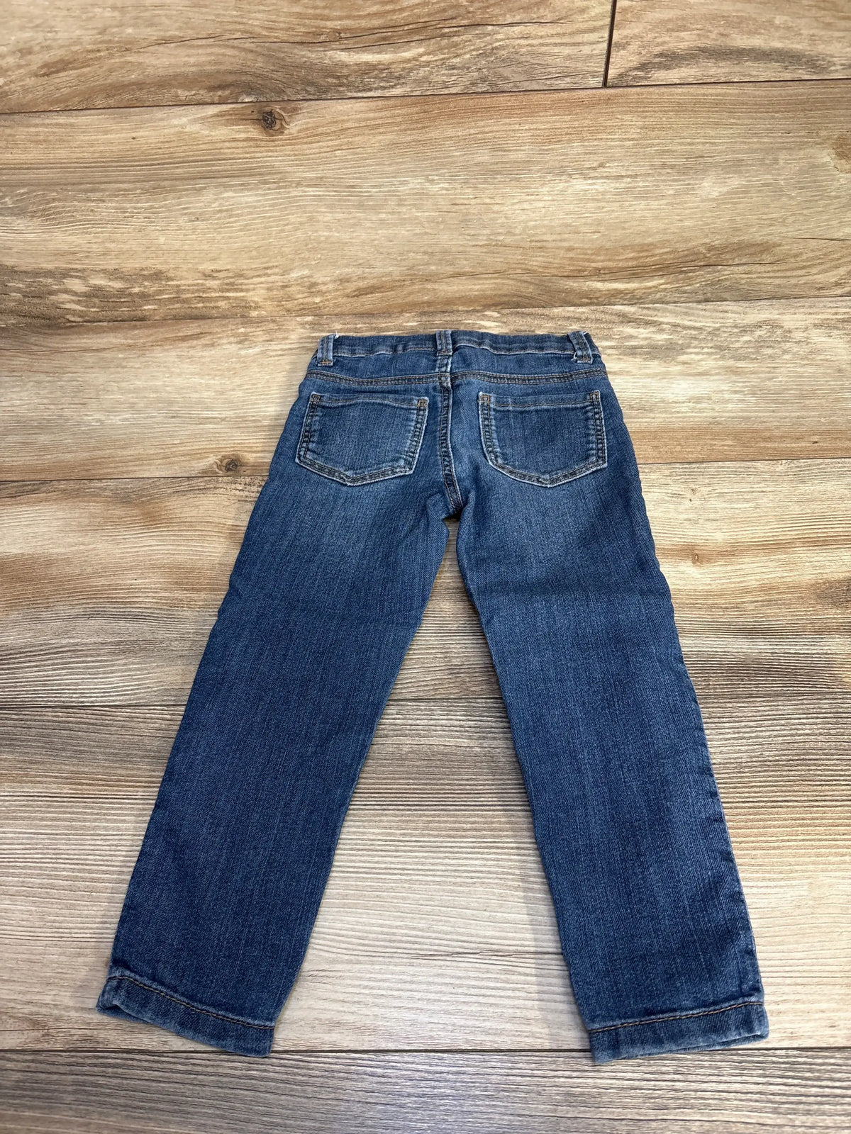 Back view of blue denim jeans with pockets laid flat on wooden floor
