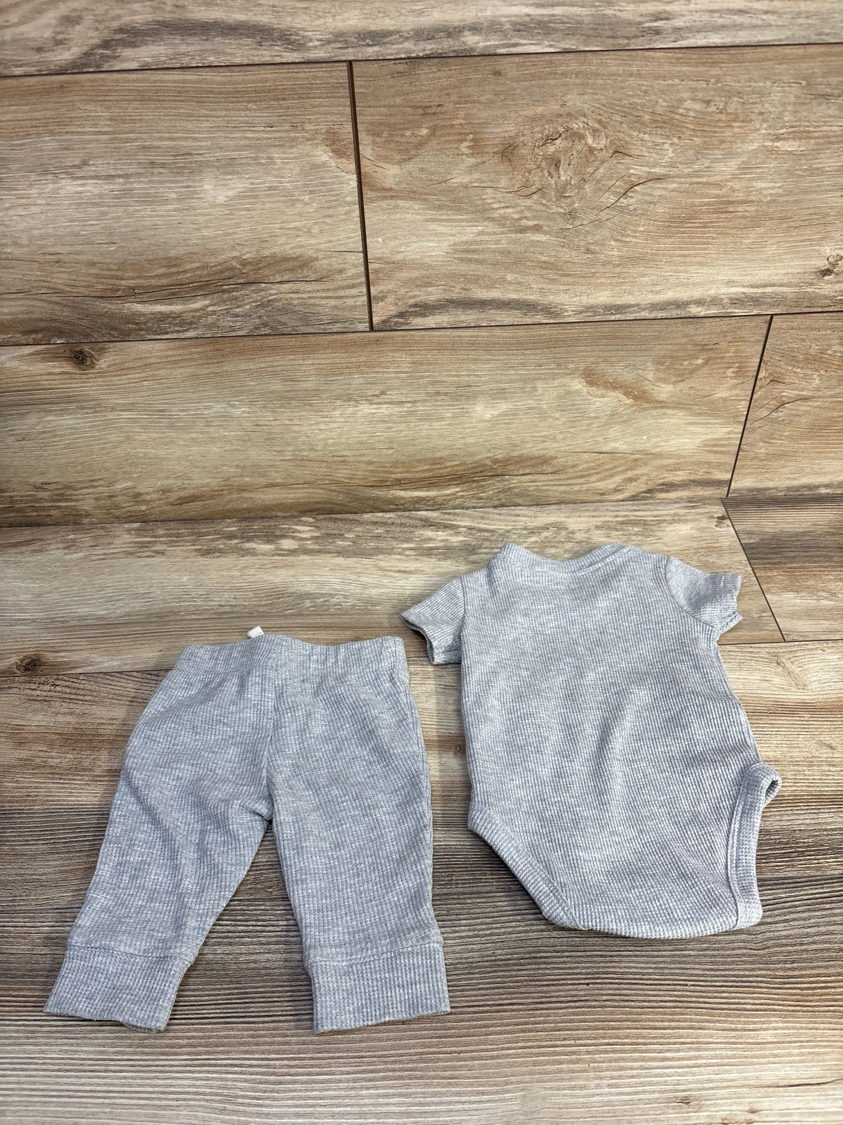 Top-down view of grey Carter's 2-piece waffle knit bodysuit and pants set laid flat showing ribbed texture on wooden floor