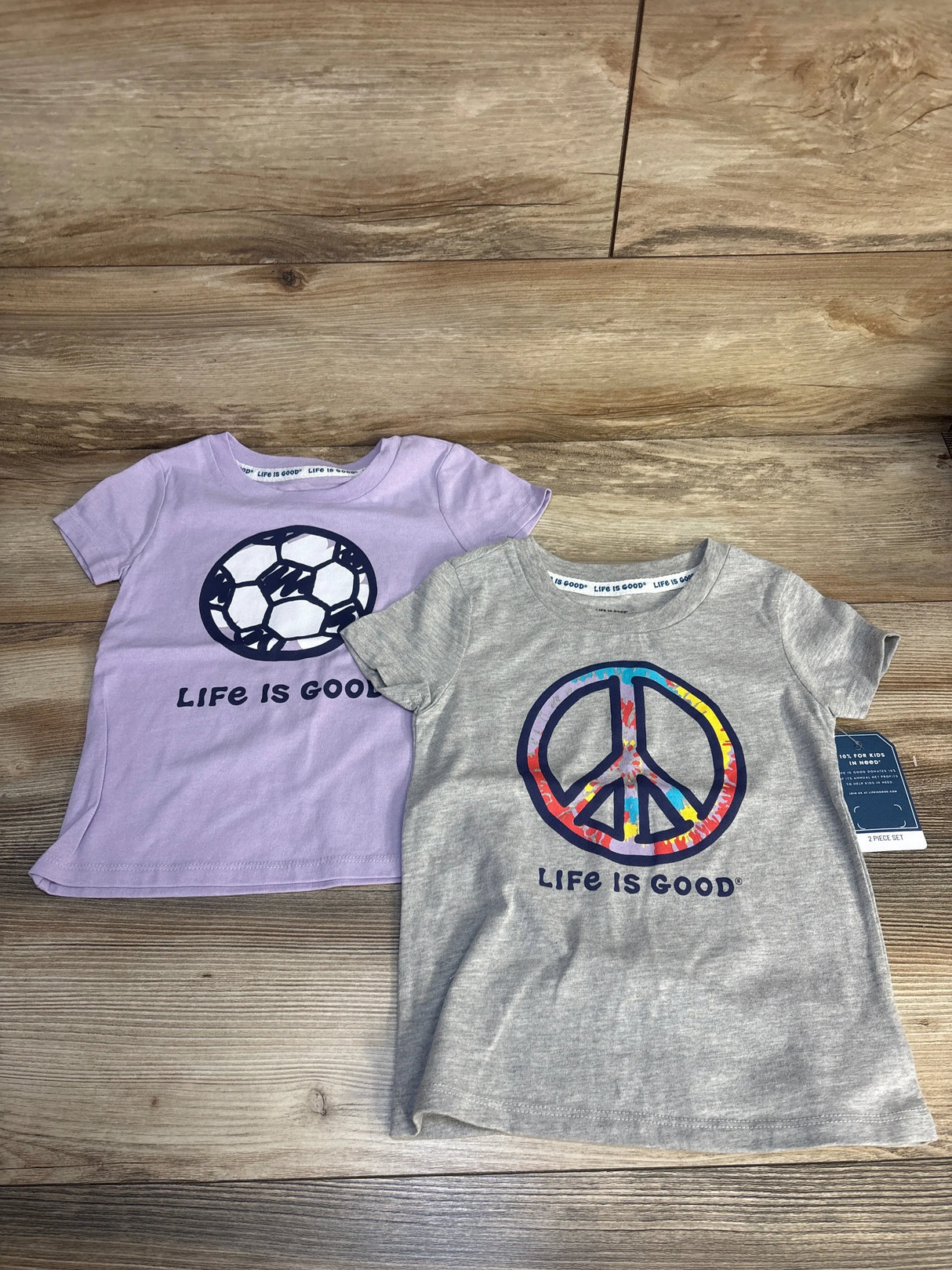 Two kids' t-shirts on wood, one with a soccer ball, one with a colorful peace sign graphic.
