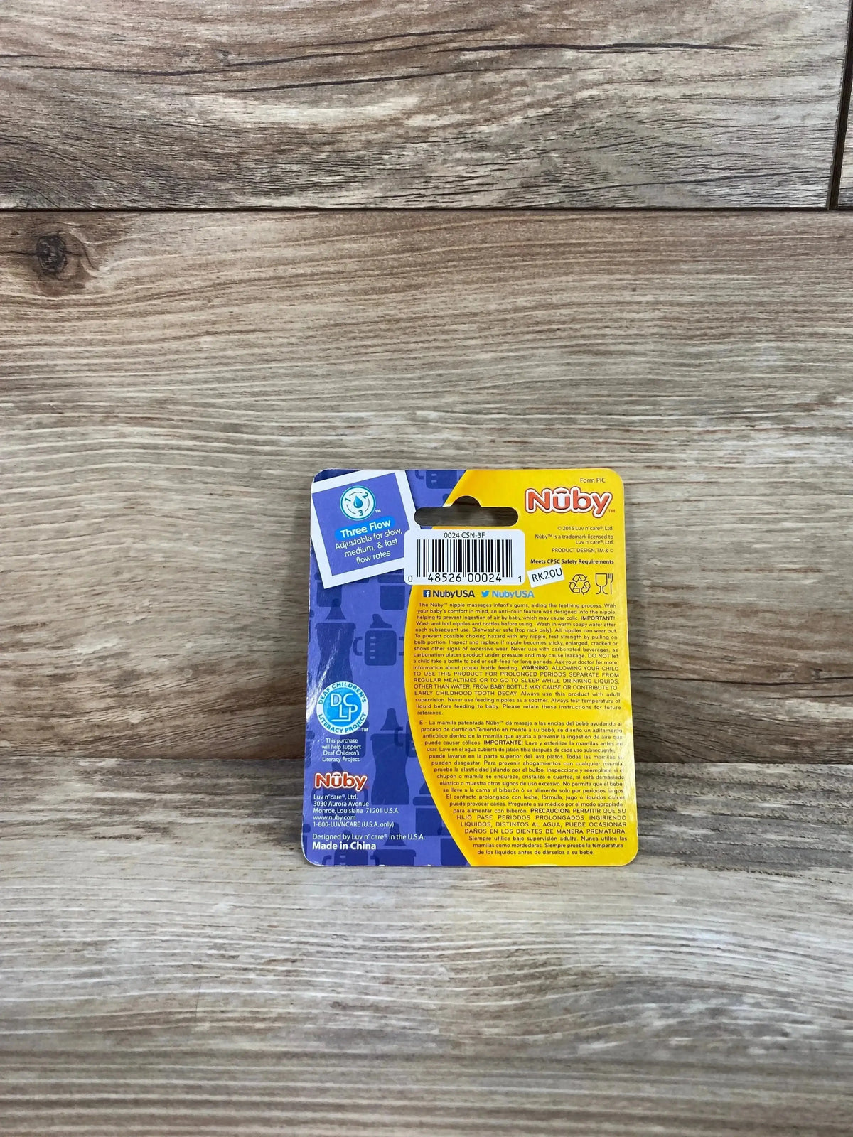Back of Nuby 2-pack Three Flow standard-neck nipples showing barcode and product info on blue-yellow packaging on wood
