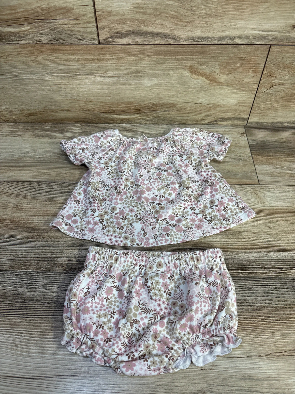 Flat lay of Nicole Miller two piece floral top and bloomer shorts set showcasing matching white floral print on wood flooring
