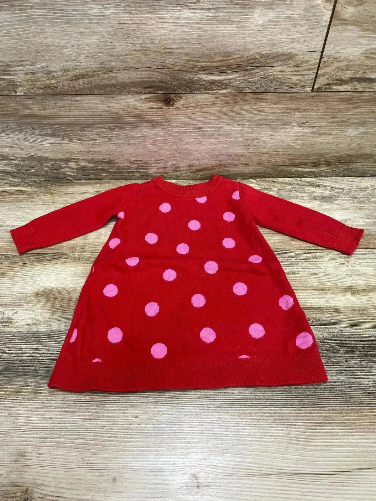Flat lay of Baby Gap toddler sweater dress showcasing red knit with pink polka dots and long sleeves on wood floor background