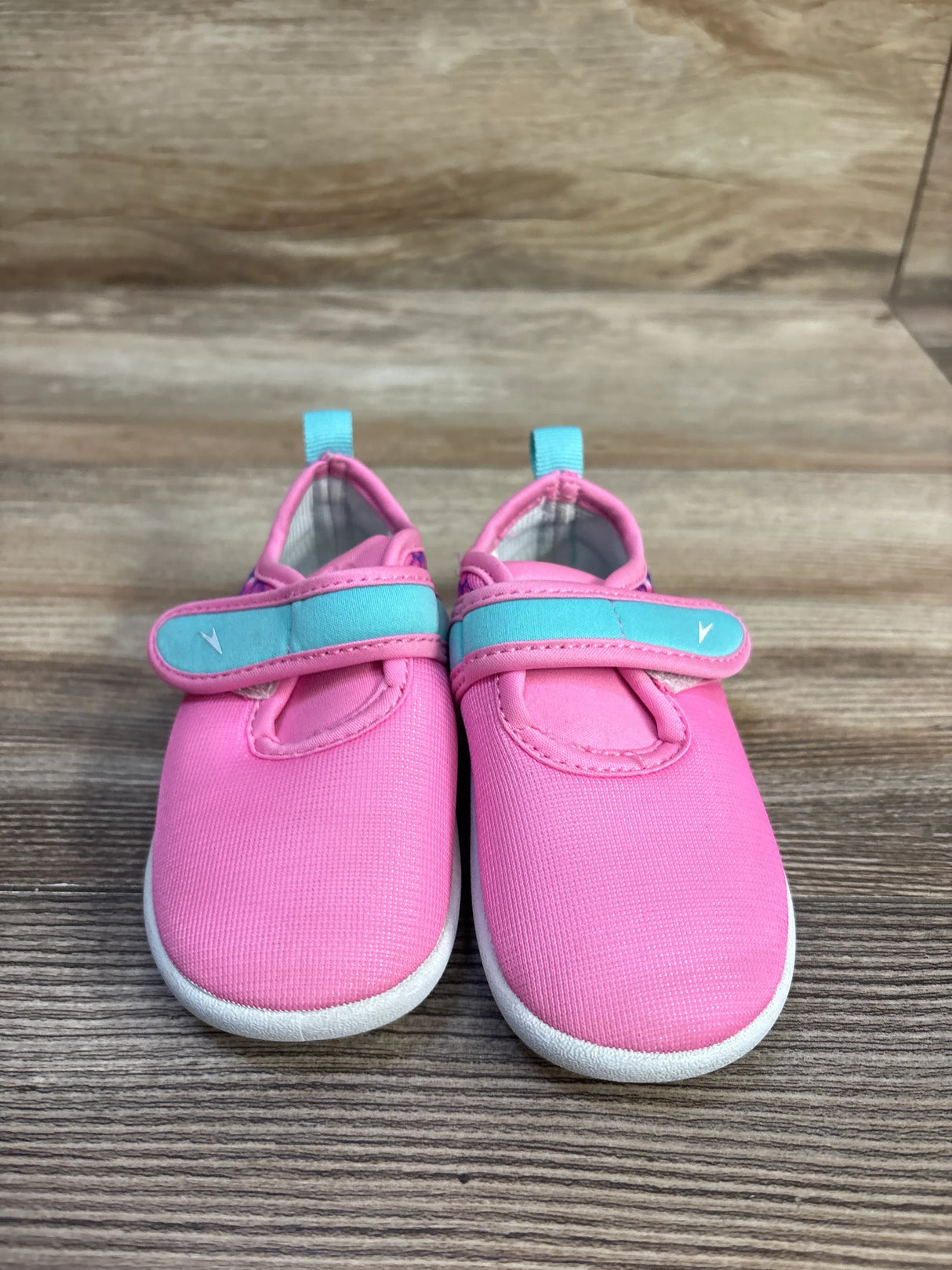 Front view of Speedo Shore Explorer kids water shoes with pink uppers, teal velcro straps, and white soles on wood surface