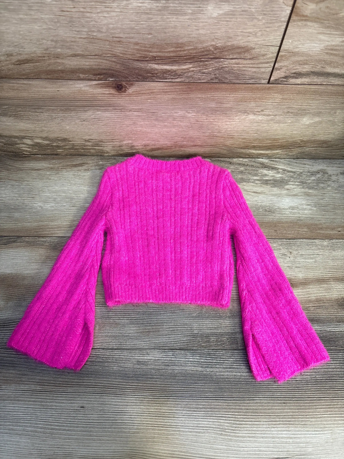 Bright pink ribbed knit long sleeve sweater for kids on wooden background