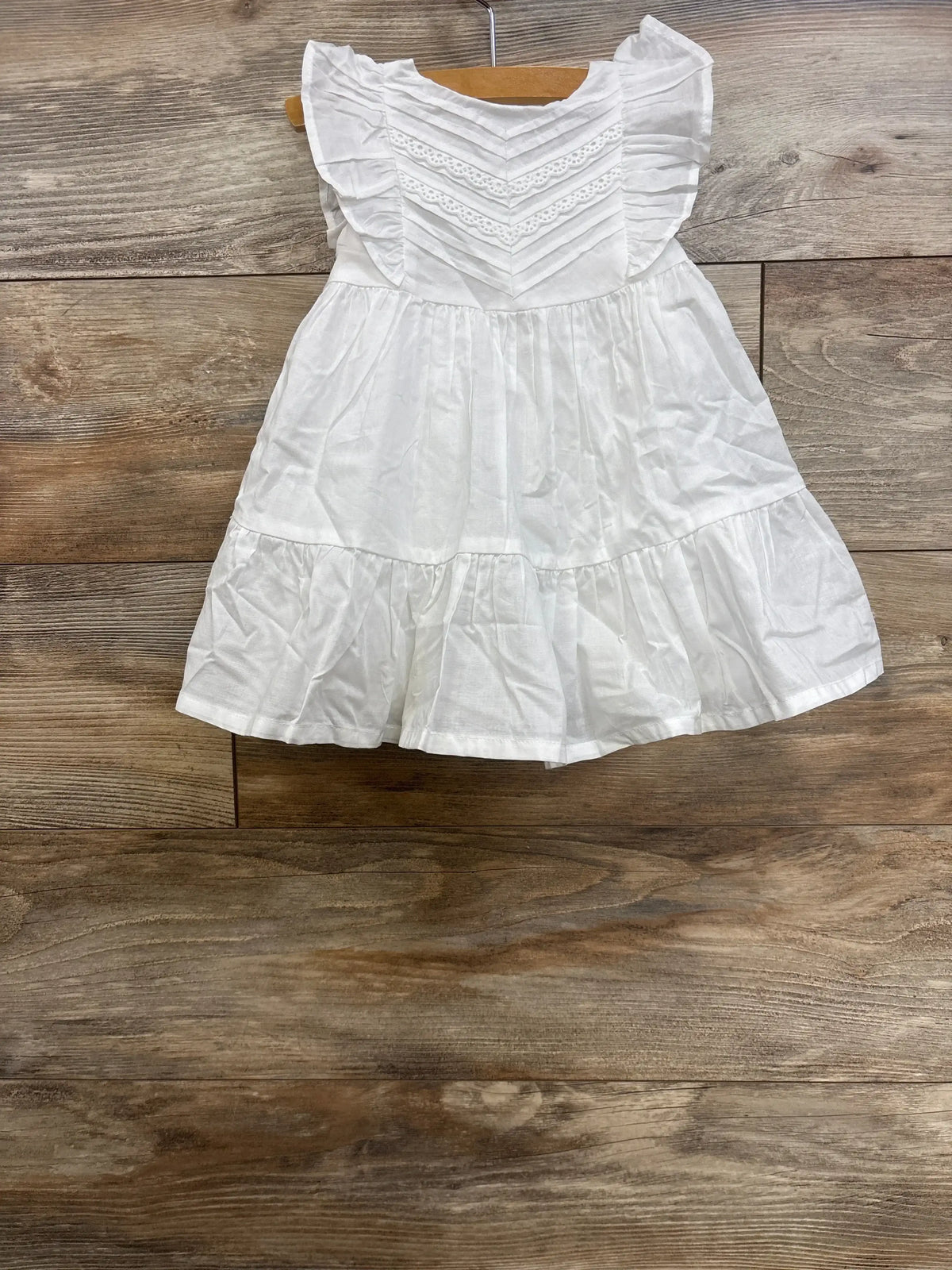 Front view of NEW OshKosh B gosh 2Pc Lace Dress in white size 12m showcasing white flutter-sleeve dress with chevron lace bodice and tiered hem on wood plank backdrop