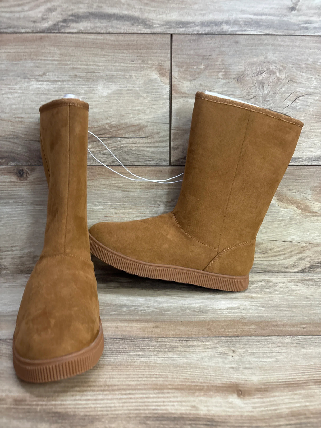Pair of brown suede winter boots with rubber soles on wooden floor background