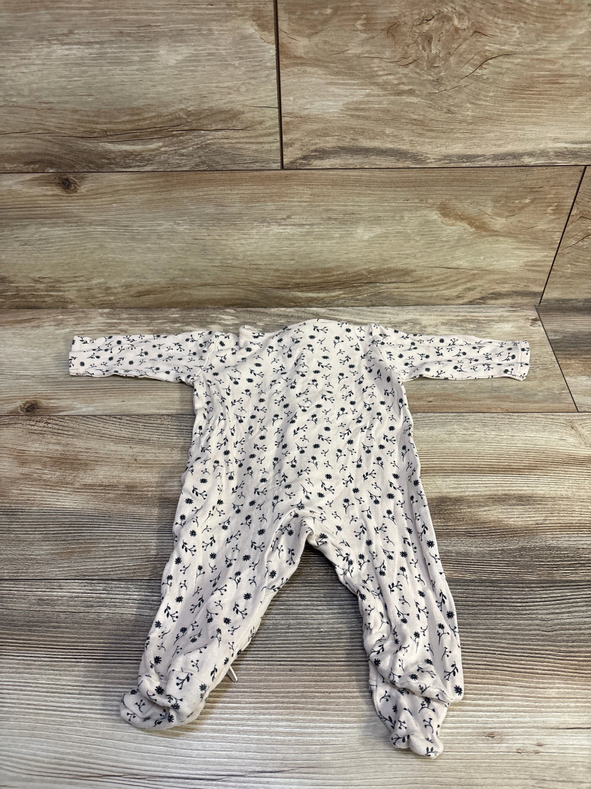 Flat lay of beige floral baby sleeper size 3M showing long sleeves, footed legs and navy flower print on wood background