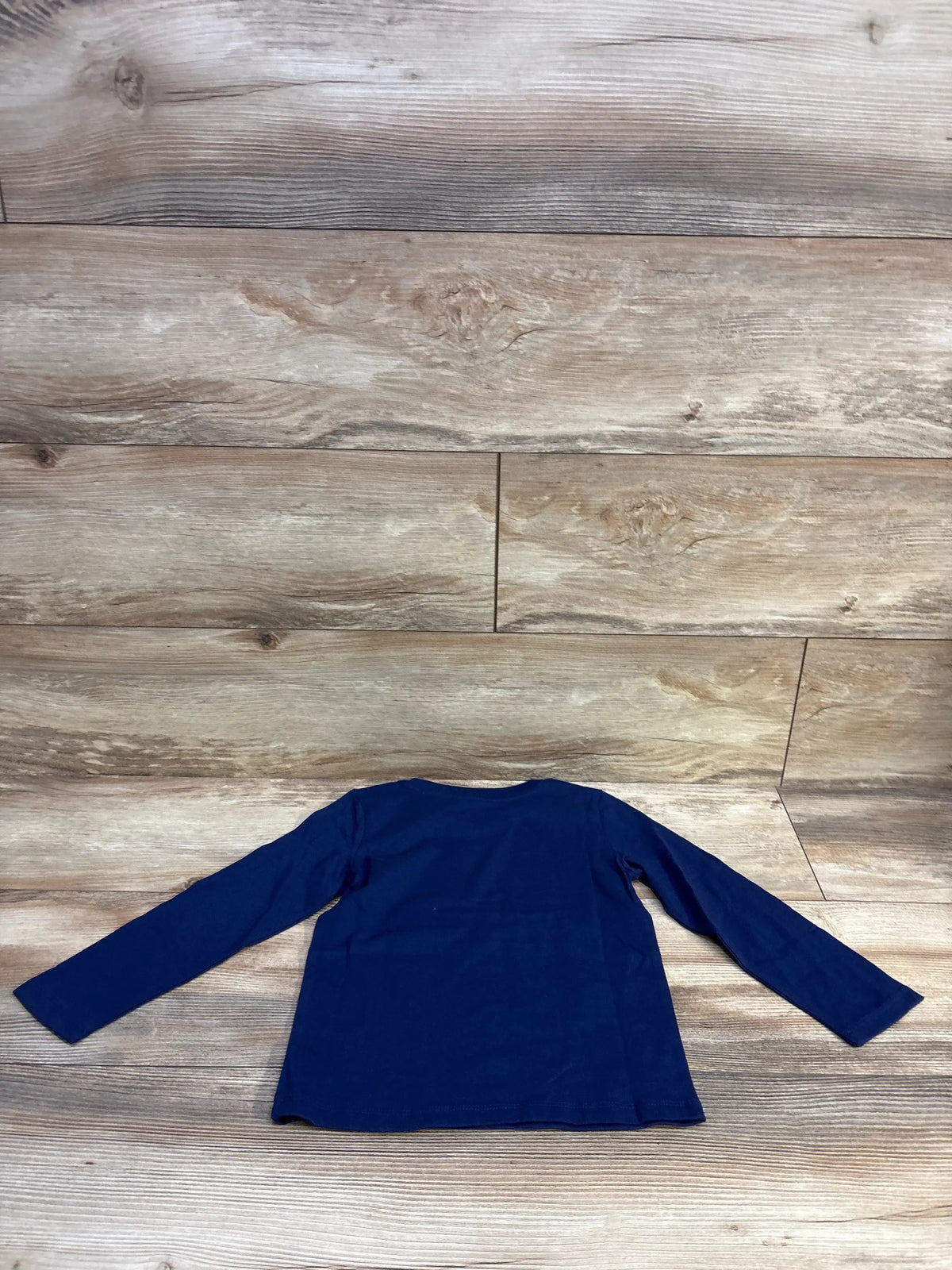 Flat-lay back view of Epic Threads navy long-sleeve toddler shirt showing solid fabric and crew neck on wood plank background