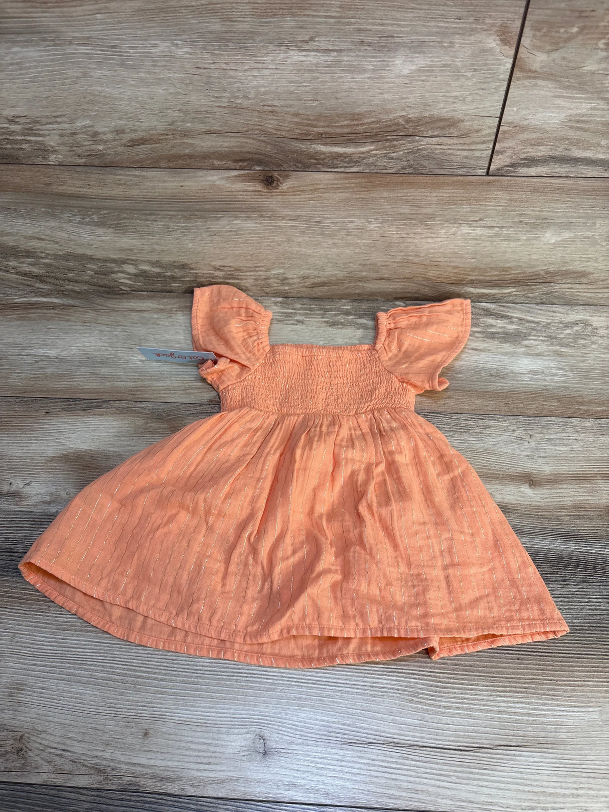 Peach toddler dress with flutter sleeves and silver stripes on wooden background