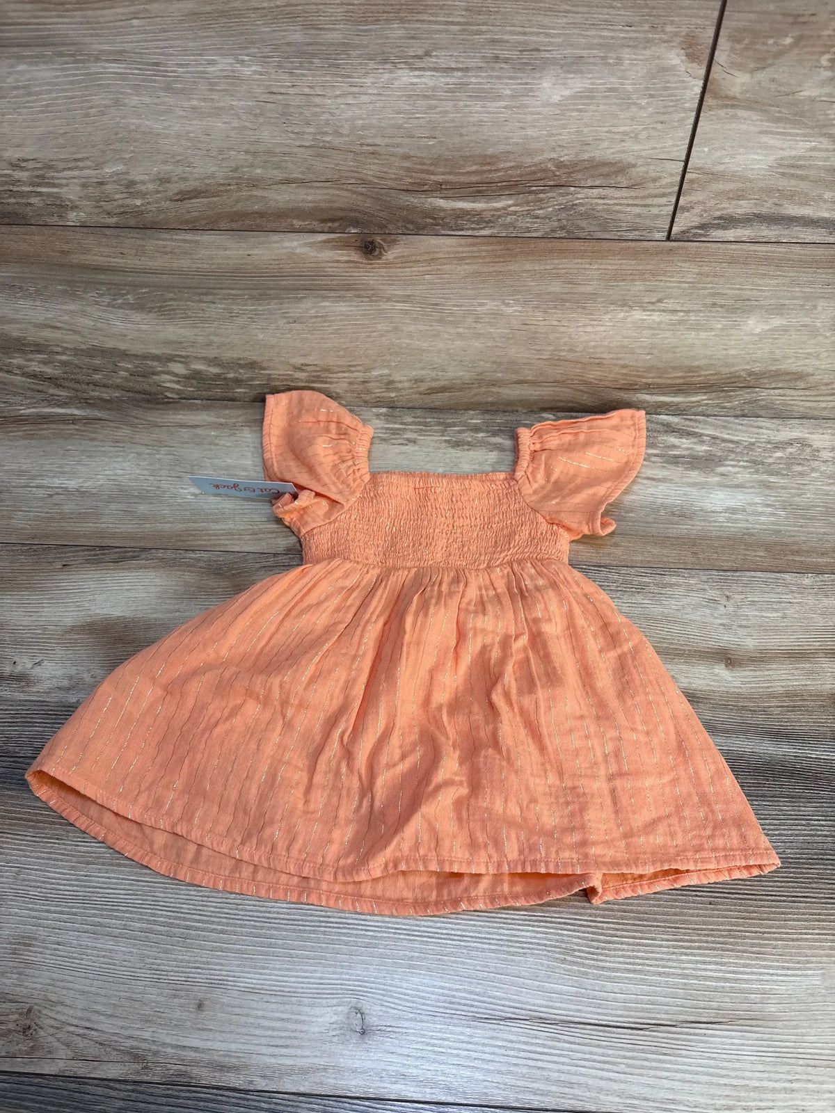 Flat lay of Cat and Jack peach gold-striped dress 18M showcasing smocked bodice and flutter sleeves on wooden floor