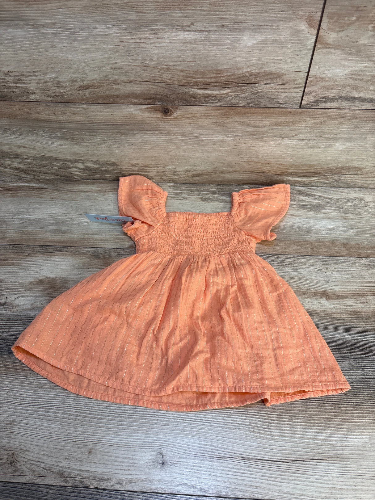 Peach toddler dress with flutter sleeves and silver stripes on wooden background