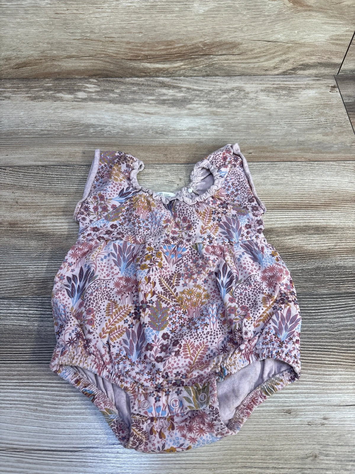 Top-down view of pink floral bubble romper showing ruffled collar, elastic leg openings, and snap closures on a light wood background