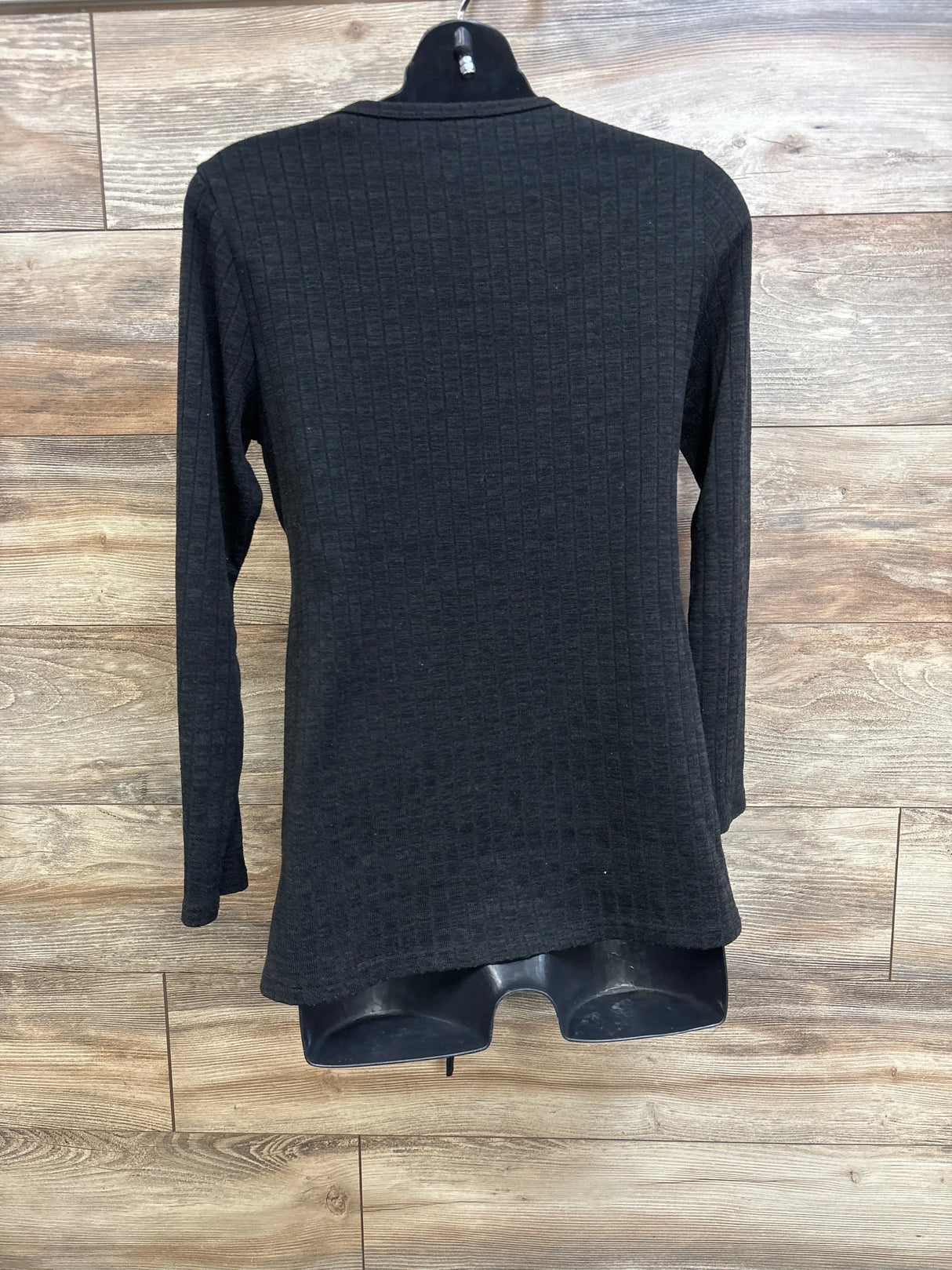 Back view of black ribbed long-sleeve maternity top with high neckline, textured knit and flared hem on wood background