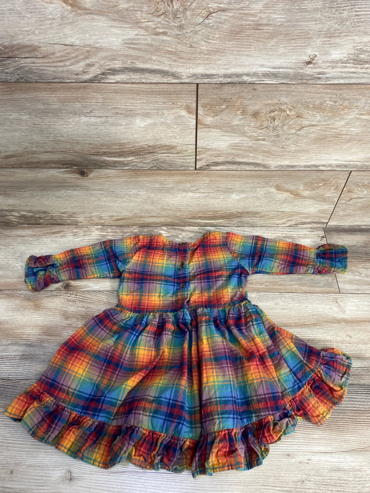Colorful plaid toddler dress with long sleeves and ruffled hem on wooden floor