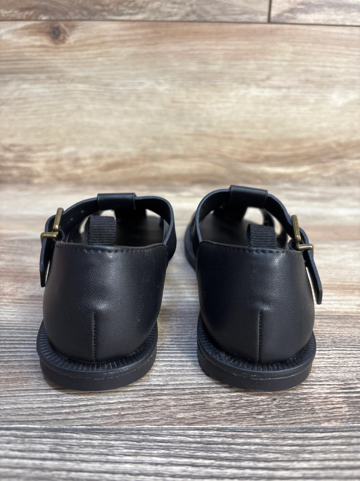 Back view of black toddler sandals with buckles on wood floor