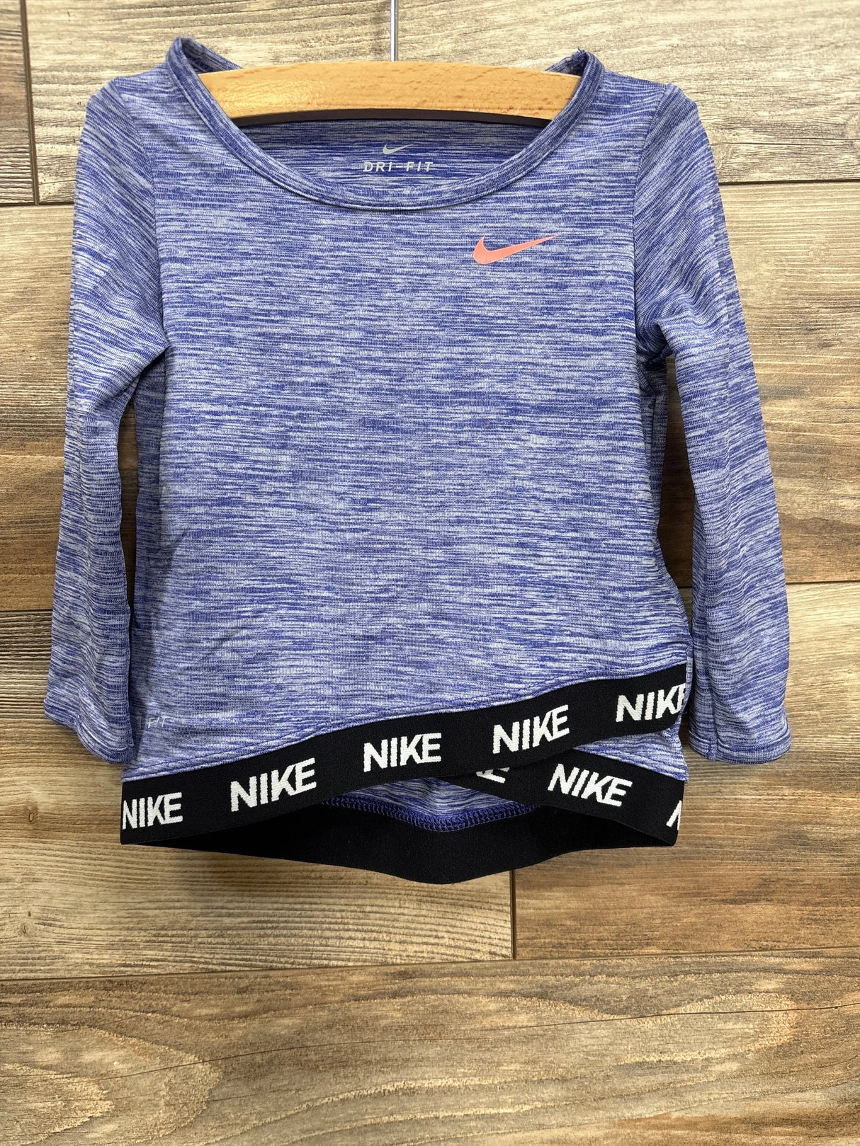 Blue Nike Dri-FIT long sleeve athletic top with black Nike logo waistband on wooden background