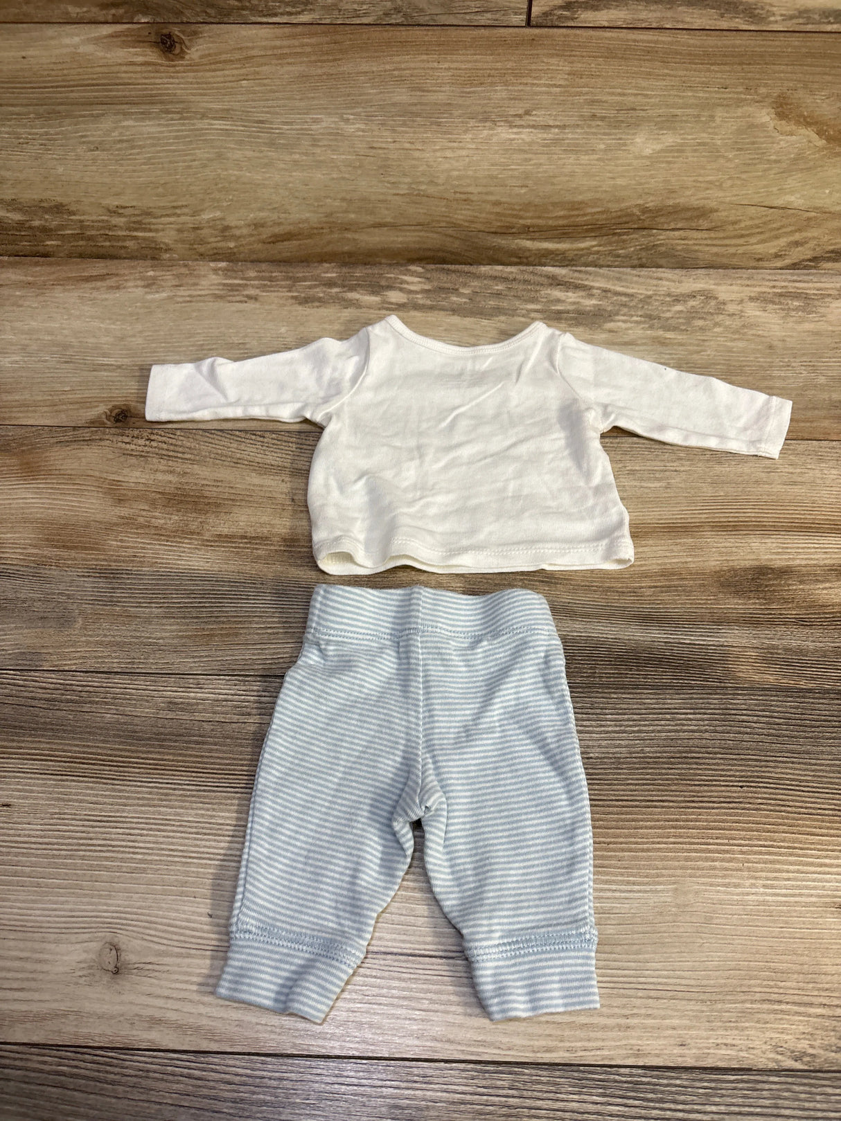 Flat lay of newborn 2-piece shirt and pants set showcasing a white long-sleeve shirt and light blue striped pants on wood background