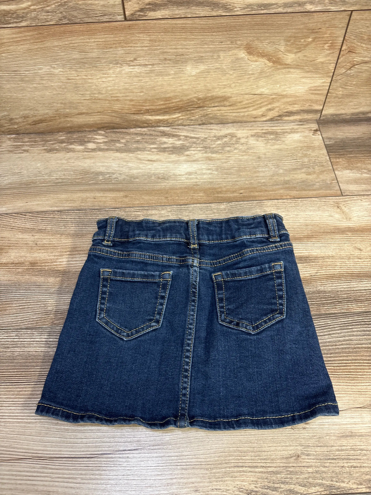 Back view of Wonder Nation denim skirt in blue, size 4-5T, showcasing two back pockets and contrast stitching on a wood floor