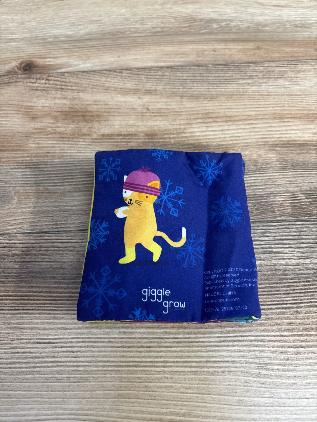 Front view of I Love Snow Crinkle Book showing a cat illustration, snowflakes, and giggle grow text on a navy cloth cover on a wooden table