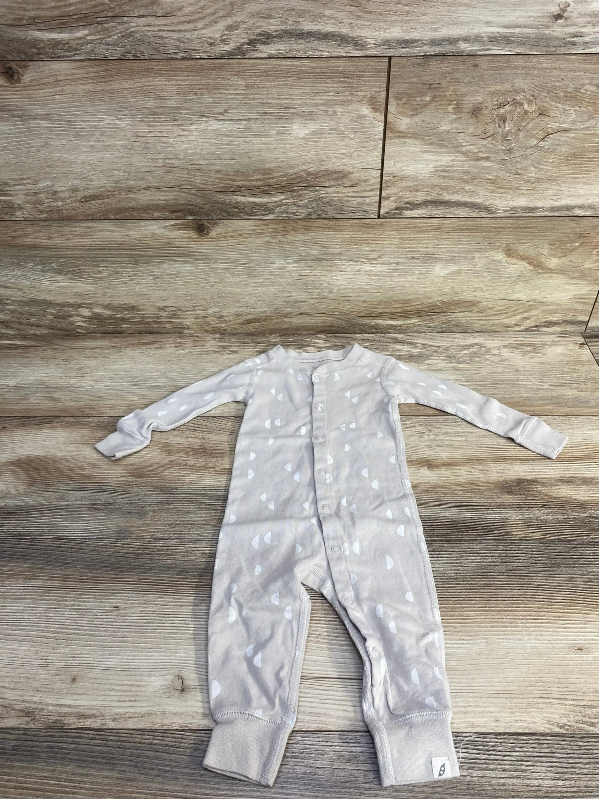 Flat lay of ivory footless sleeper, 12 months, with front snaps, long sleeves and white semicircle print on wood background