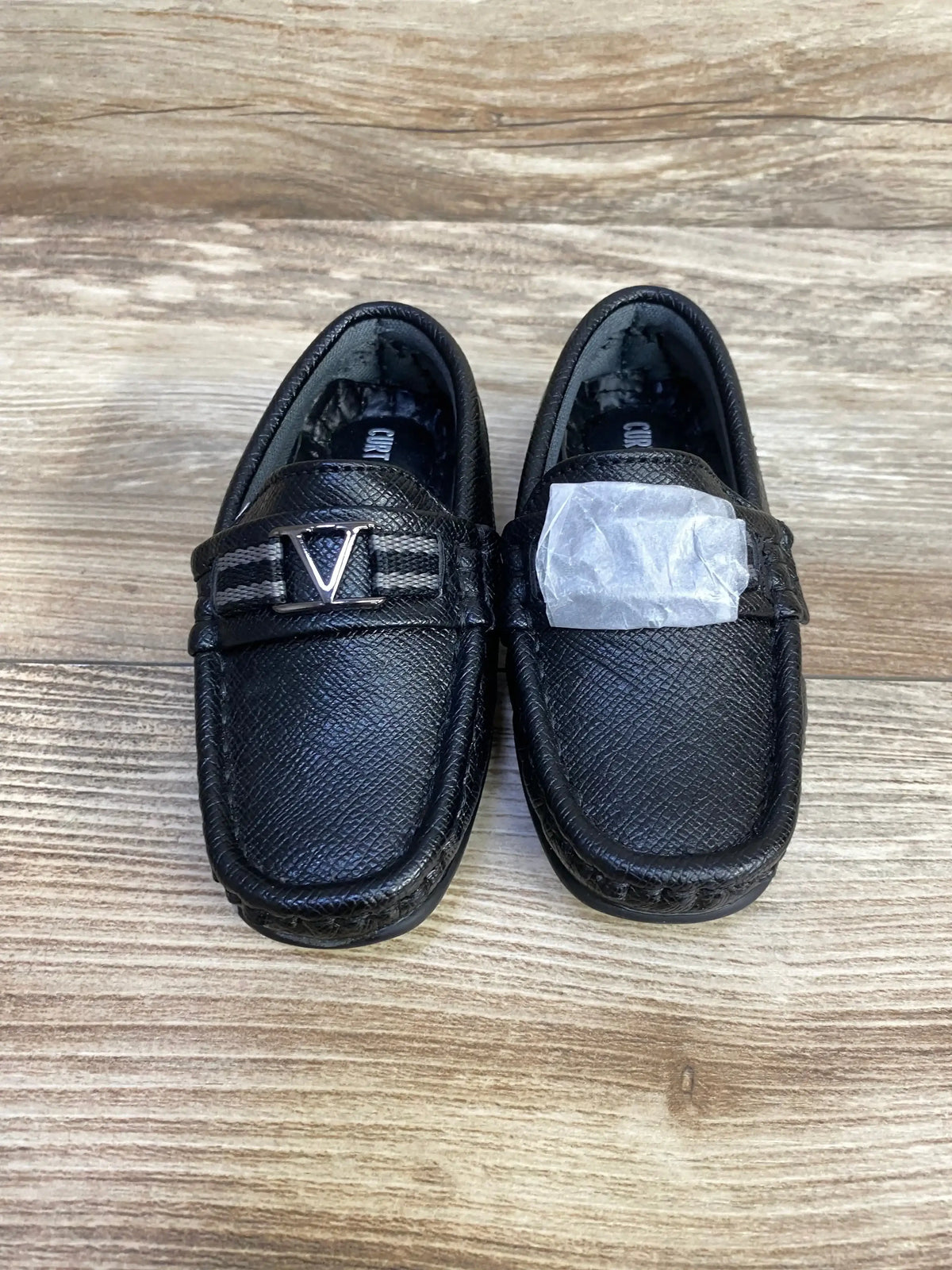 Top view of Curt and Larson black loafers showcasing textured leather V hardware strap and stitched moc toe on wood plank floor