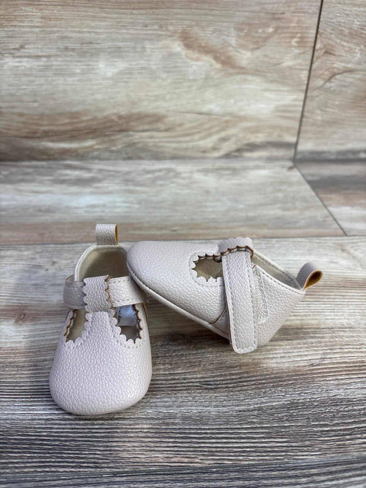 Front and side view of First Steps beige soft sole baby shoes showing scalloped T-strap on wood background