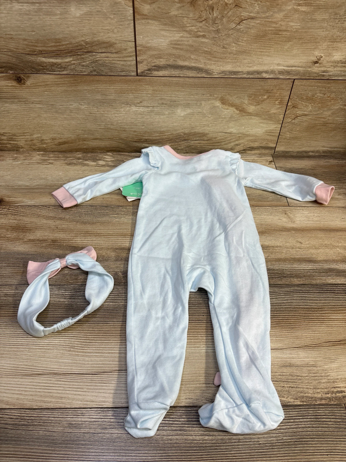 Top-down view of Dumbo 2-piece pale blue footed sleeper with pink trim and matching headband on wood background