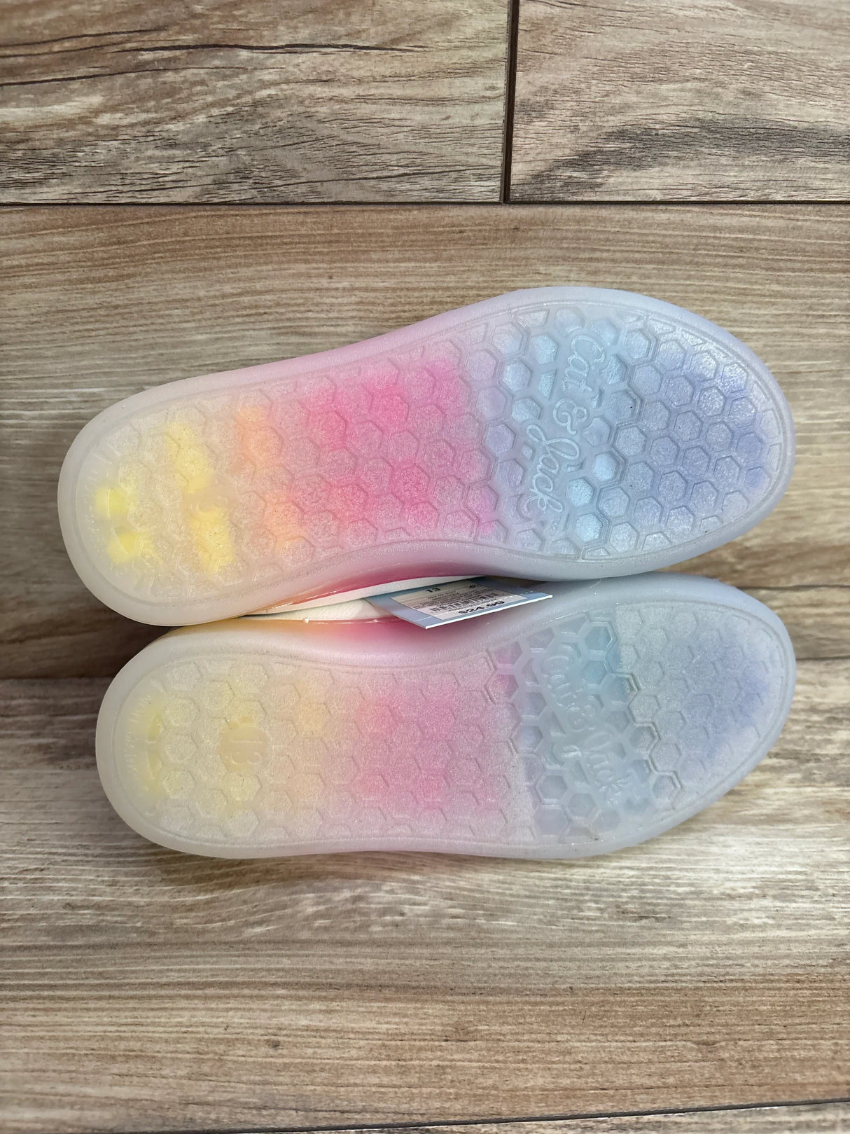 Bottom view of Cat & Jack Kira kids’ sneakers showing translucent rainbow hexagon-patterned soles on wood floor