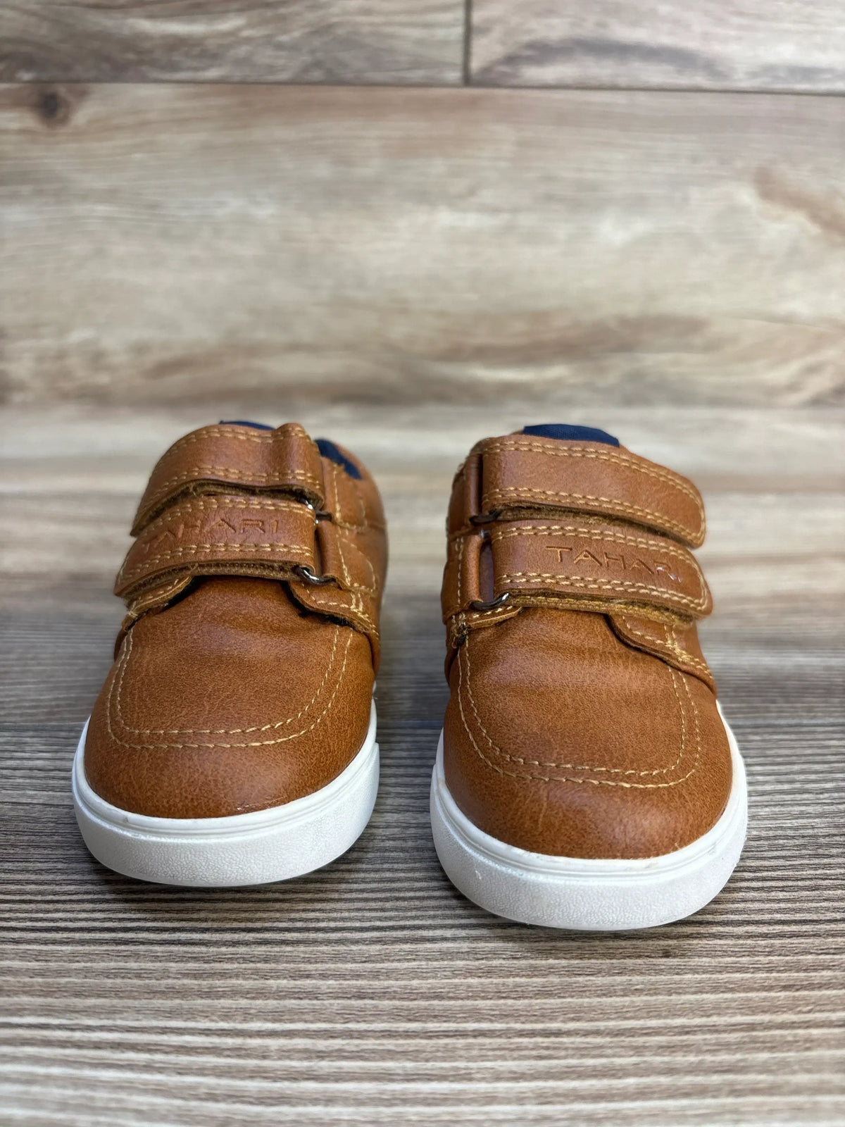 Tan Tahari toddler shoes with velcro straps, white soles, navy accents on wood floor