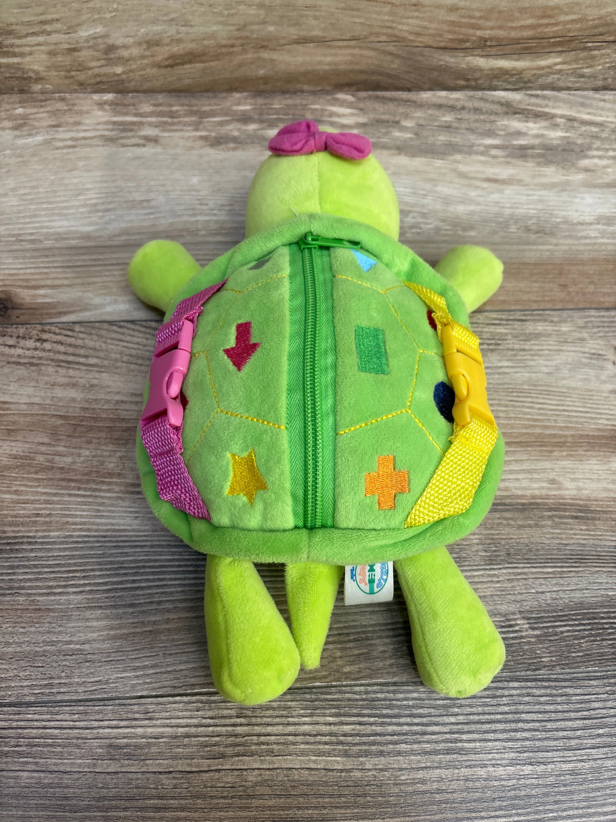 Green plush turtle toy with zipper, colorful buckles, and geometric shapes on shell