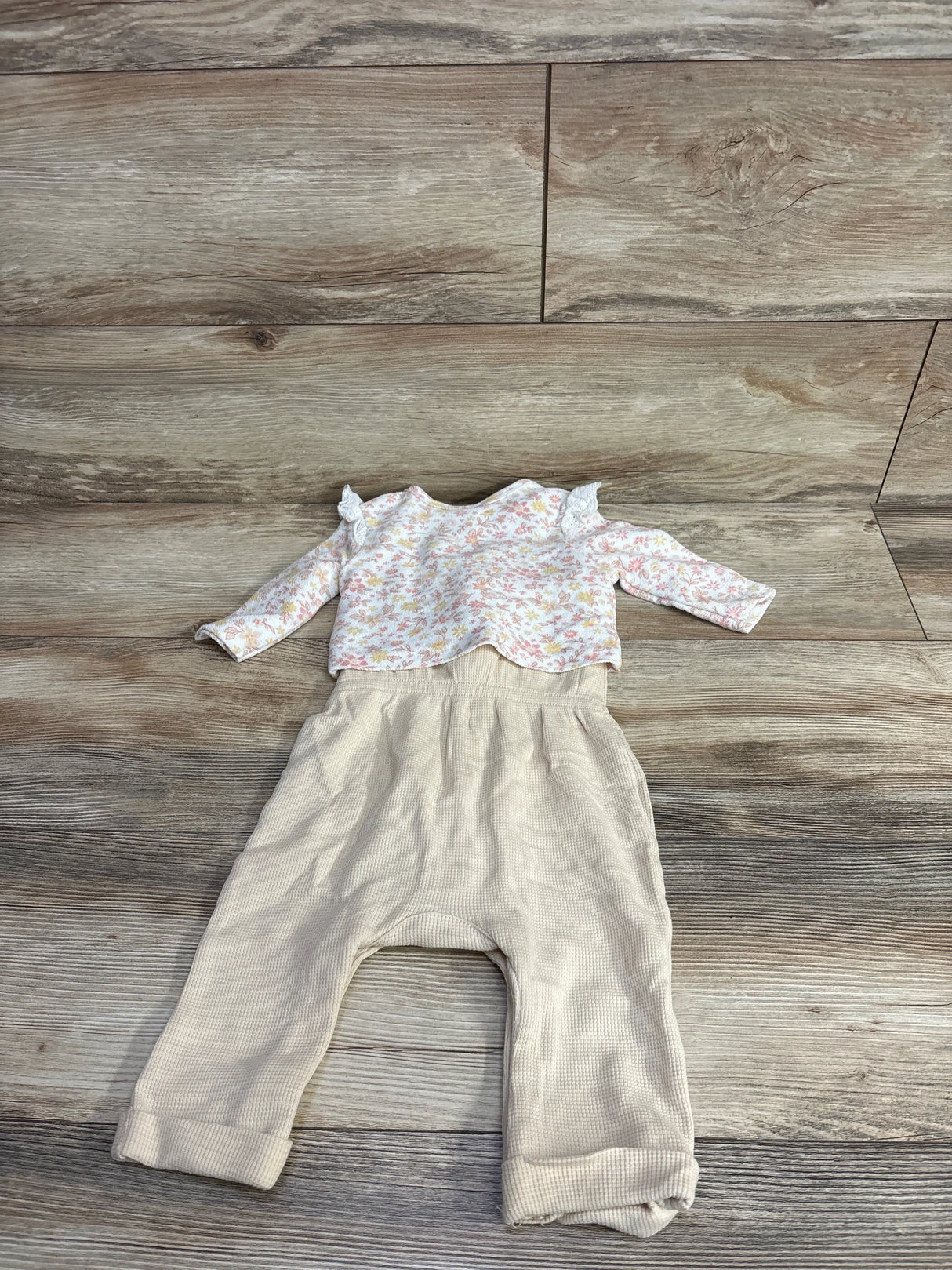 Flat lay of Nicole Miller 2-piece floral button-front cardigan set showing ruffled-shoulder floral top and beige ribbed pants on wood floor