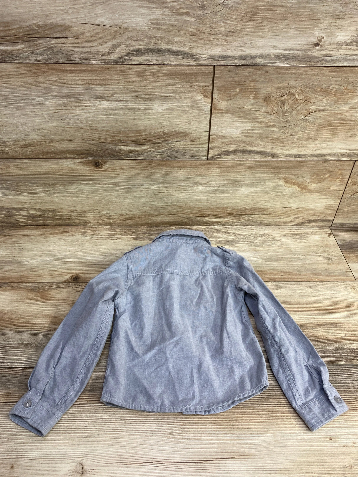 Back view of a long sleeve light gray denim toddler shirt on wood background