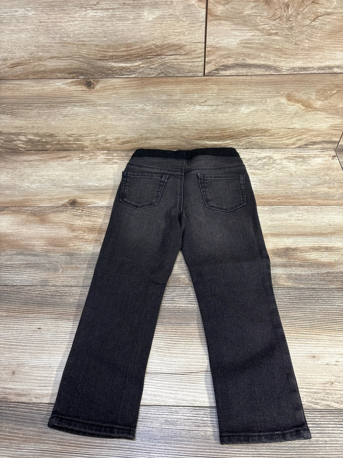 Back view of black toddler rib-knit skinny jeans showing elastic waistband, two back pockets and distressing on wood floor