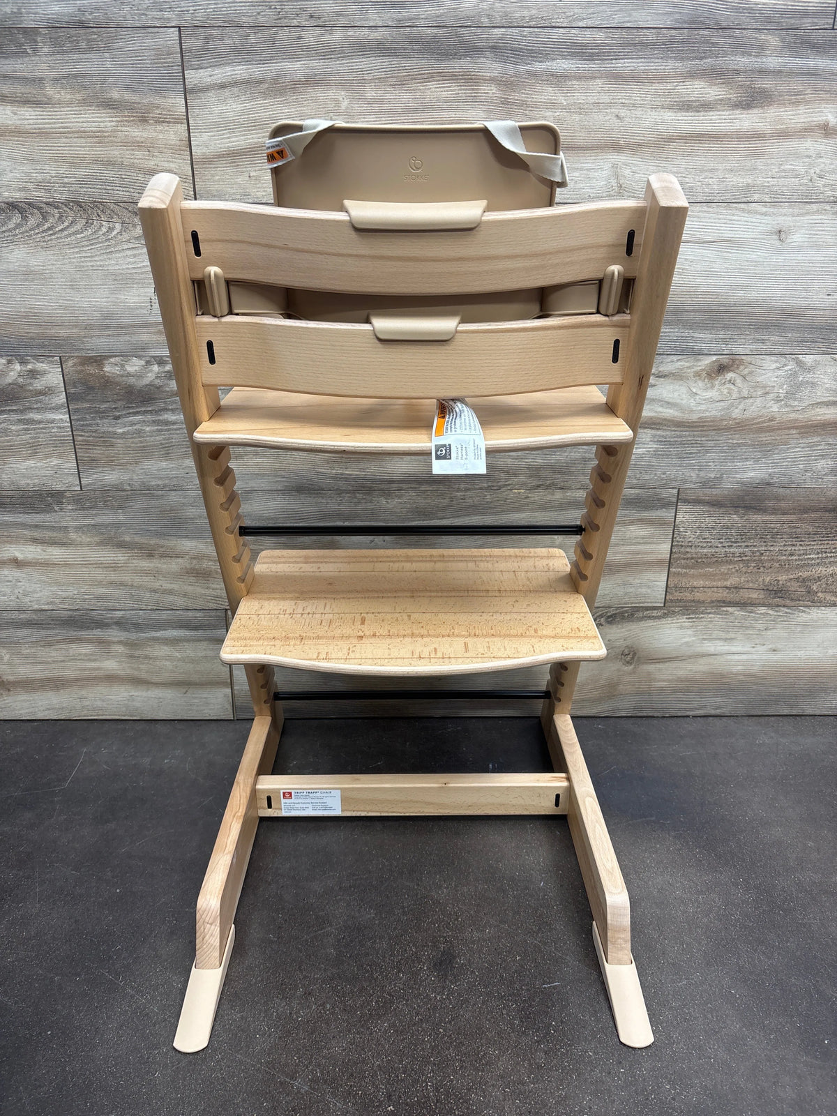 Front view of Stokke Tripp Trapp high chair with tray in Wild Wood Natural showcasing adjustable footrest with wood-panel background