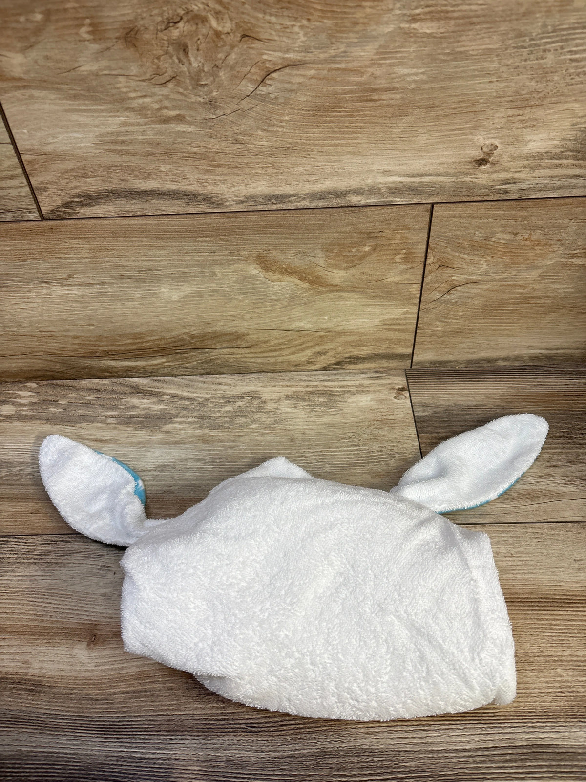 Top view of hooded white baby bath towel with bunny ears showing blue inner ear lining on wood floor background