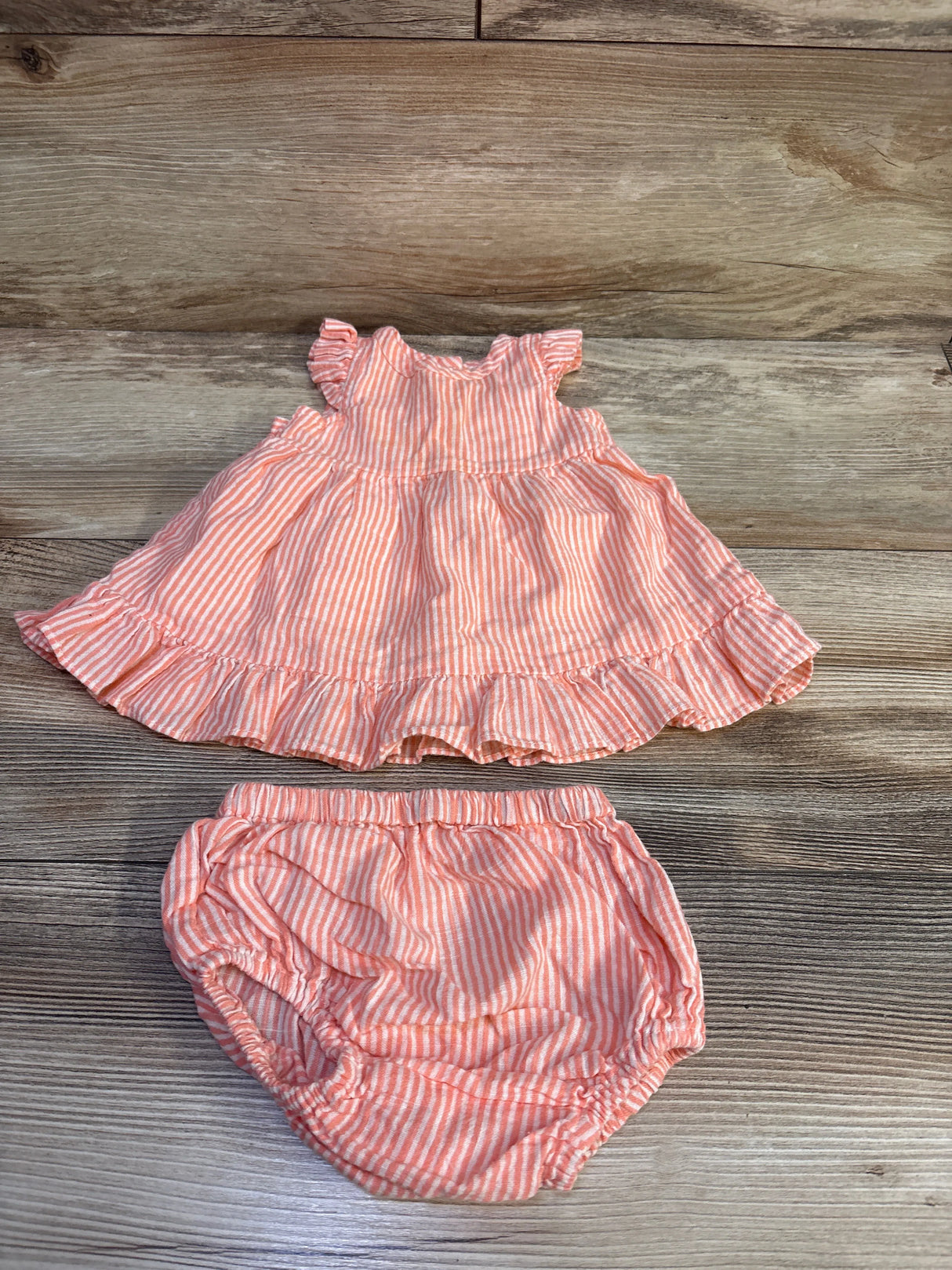 Top-down view of coral striped sleeveless baby dress and matching bloomers with ruffled hem and elastic waist