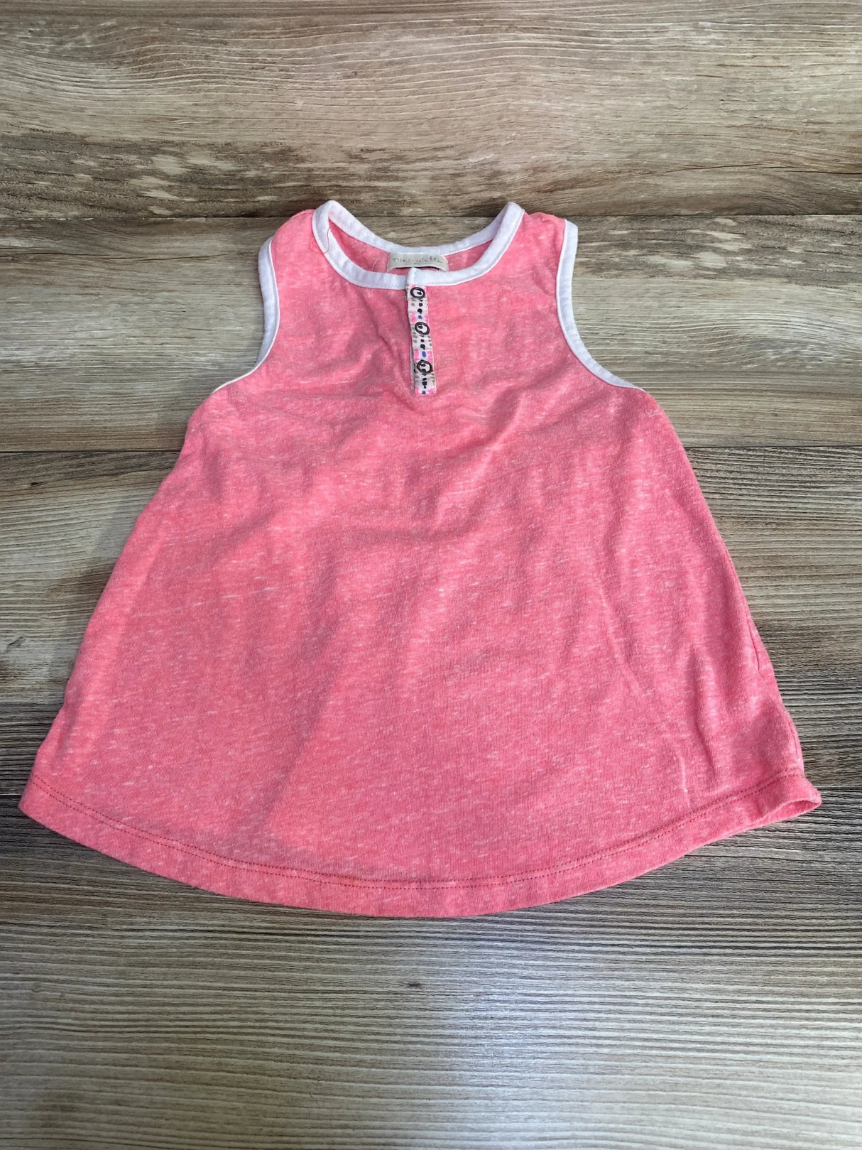 Flat lay of Miki Miette pink 4T tank top showing A-line shape, white trim and button placket on wood background