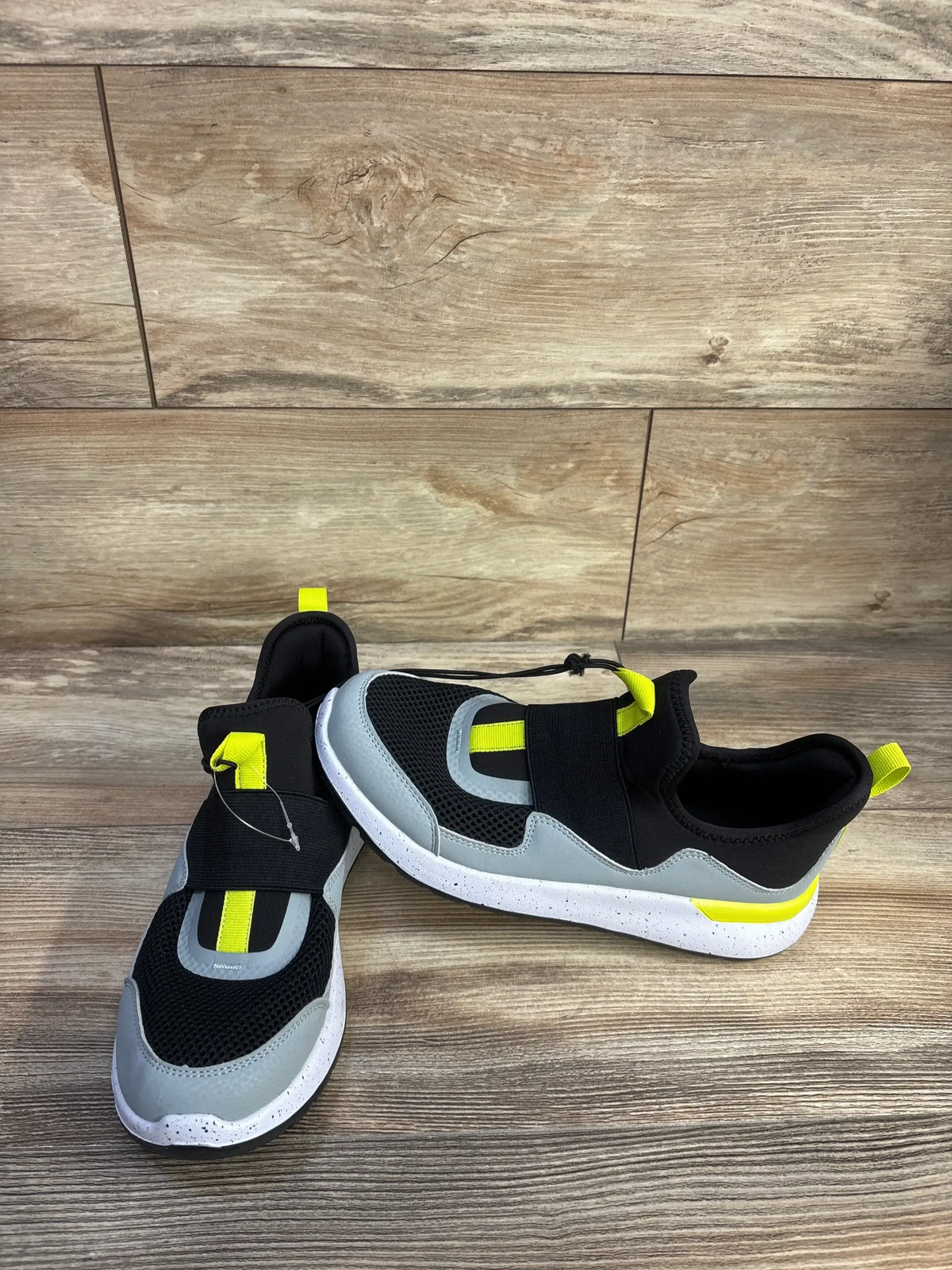 Angled overhead of All in Motion Fern slip-on sneakers with grey and black mesh, neon yellow pull tabs, speckled white soles on wood floor
