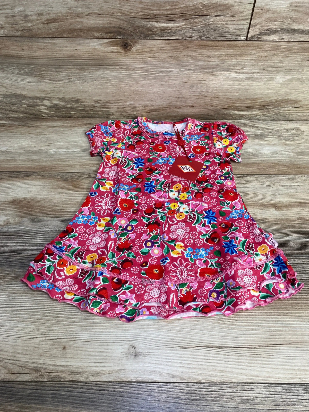 Flat lay of Oilily pink toddler dress size 2T showing short sleeves, ruffle hem and multicolor floral print on wood background