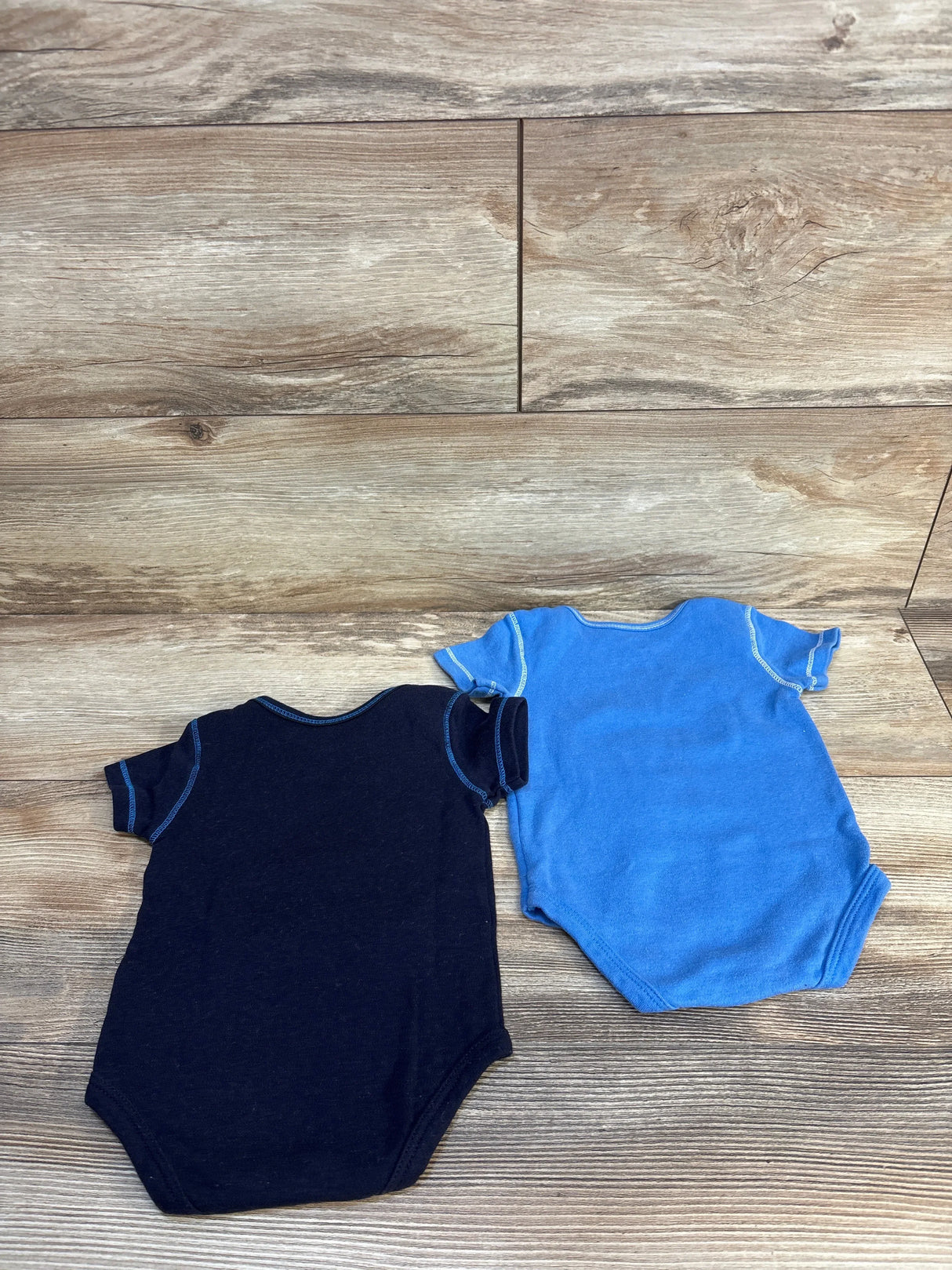 Two short-sleeve baby bodysuits in navy and blue on wood background, kids clothing